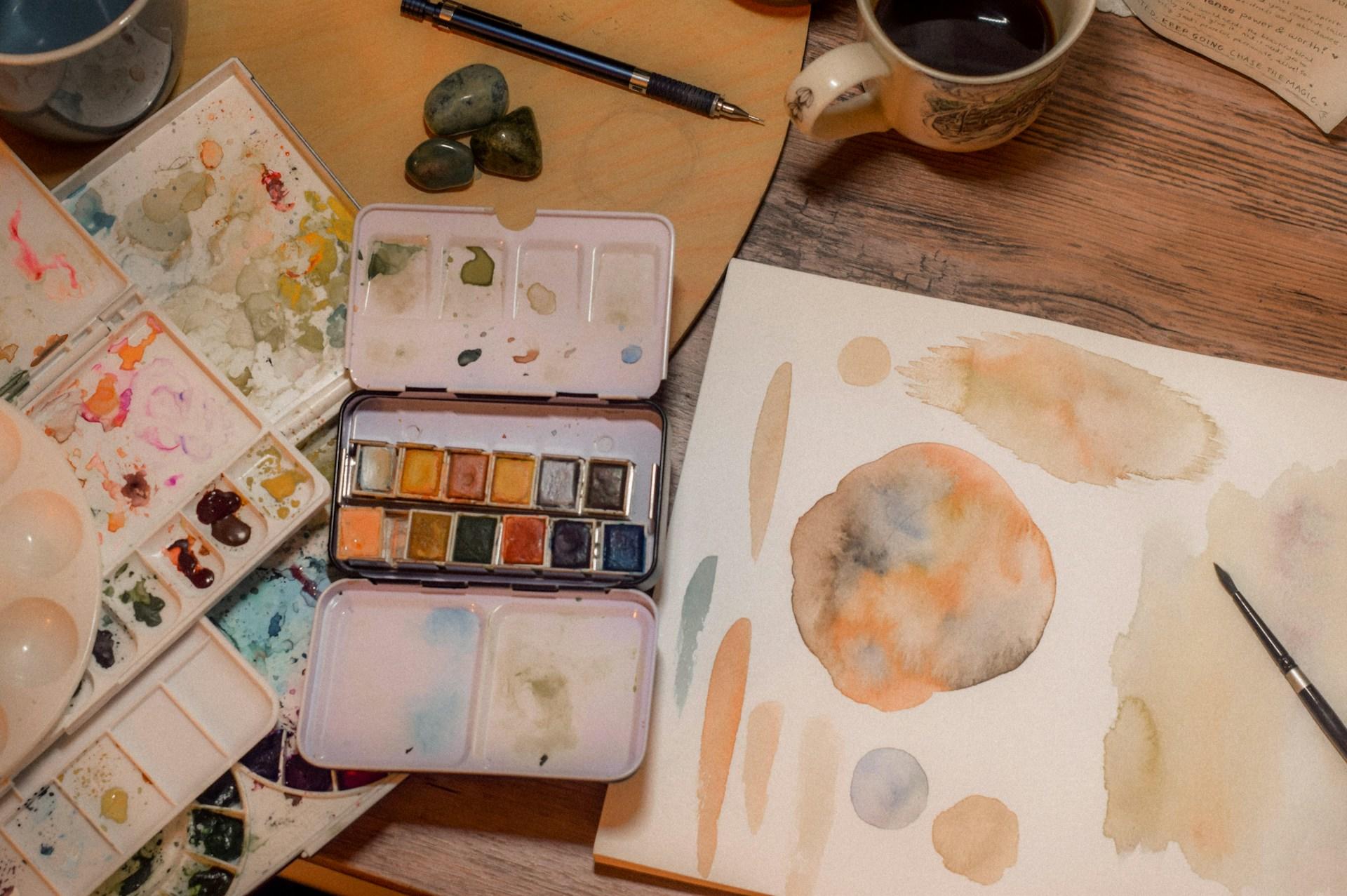 A table displaying watercolor paints, brushes, and a cup of coffee