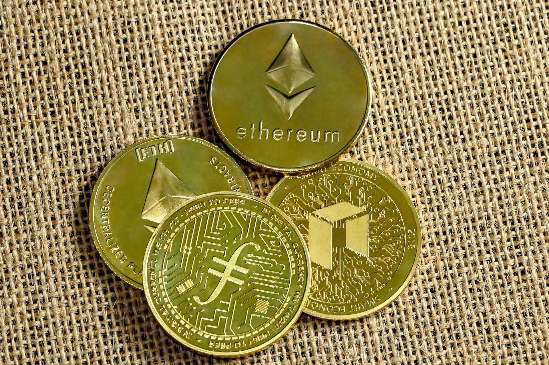 Four golden cryptocurrency coins laying on a brown jute mat.