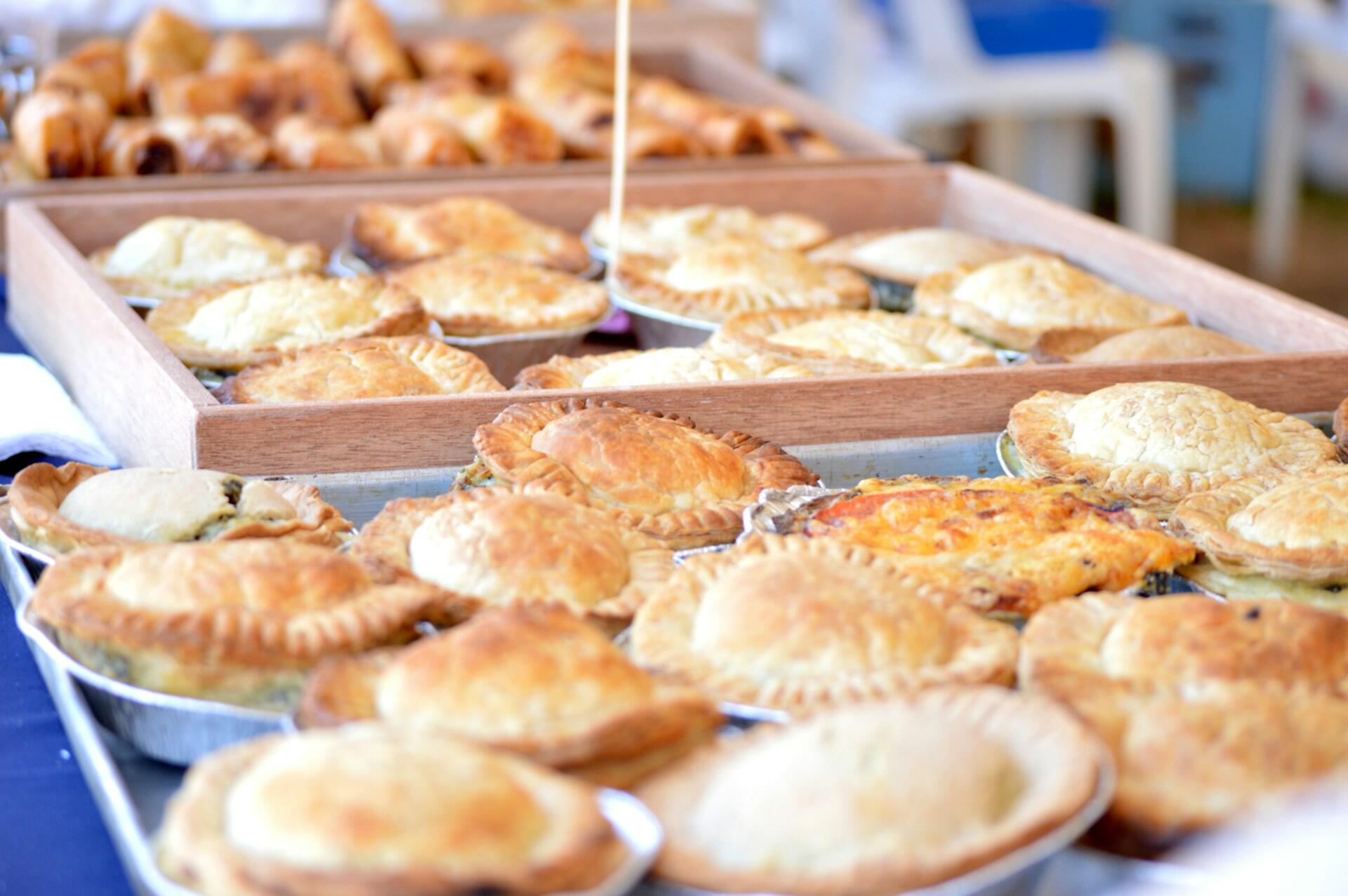 A variety of golden meat pies displayed on trays.