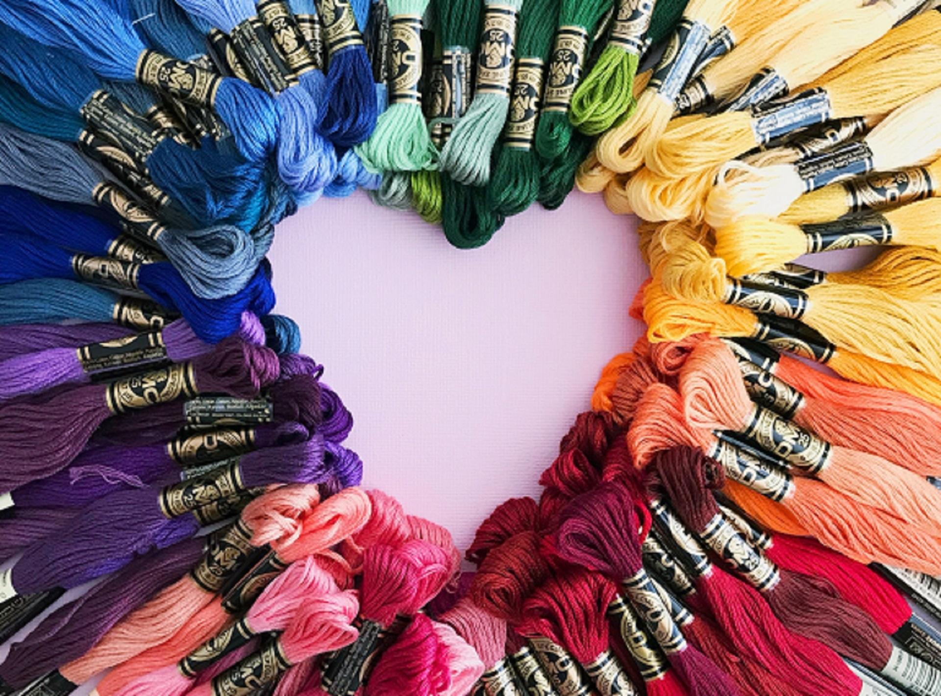 A colourful array of embroidery thread arranged so that they draw a heart with the tips of their skeins.