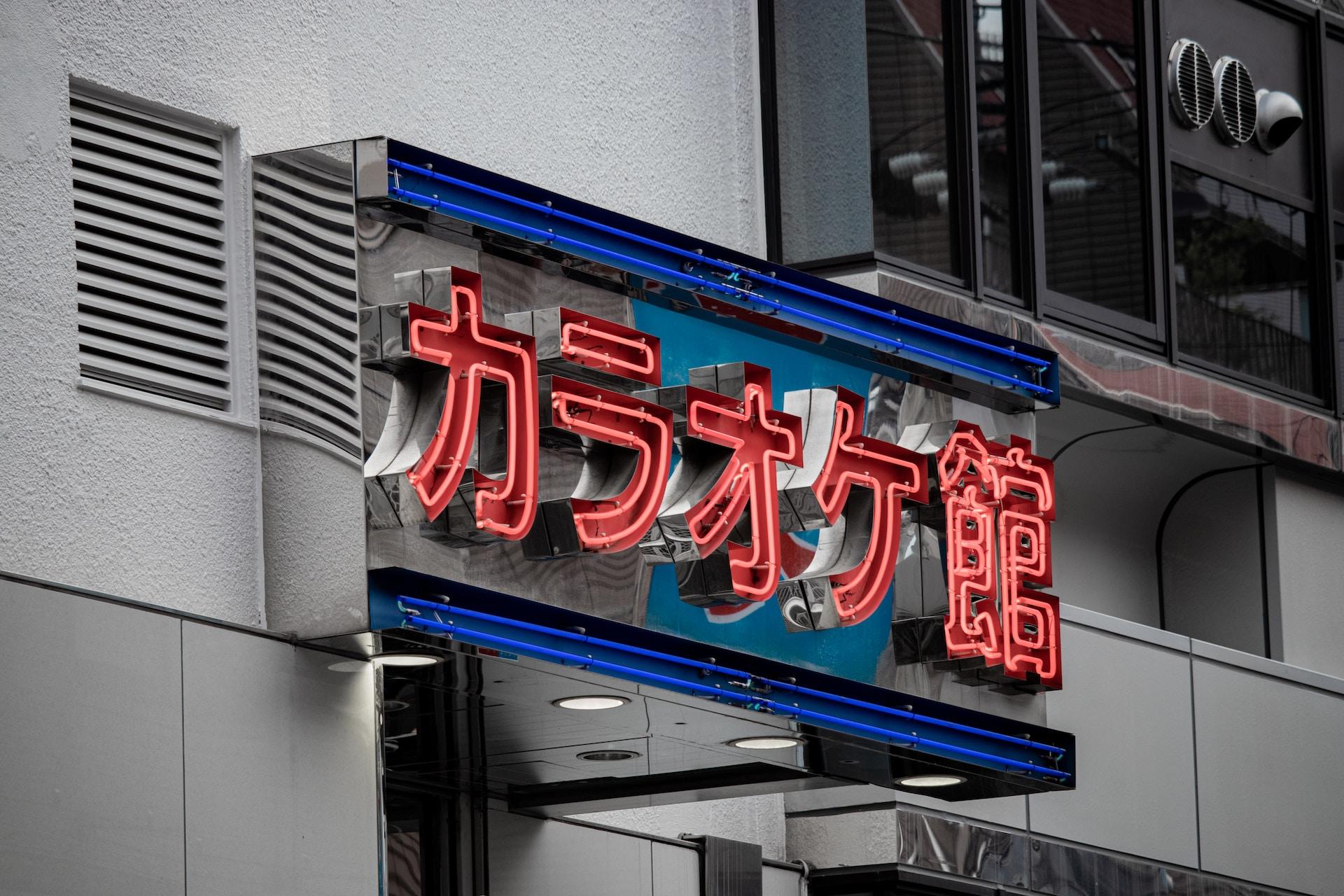A sign written in Japanese with its characters in red and blue lines framing the writing on the top and bottom. 