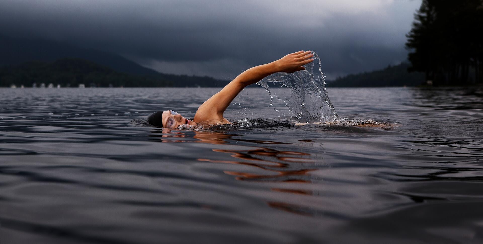 A person swims outdoors on a cloudy day. 