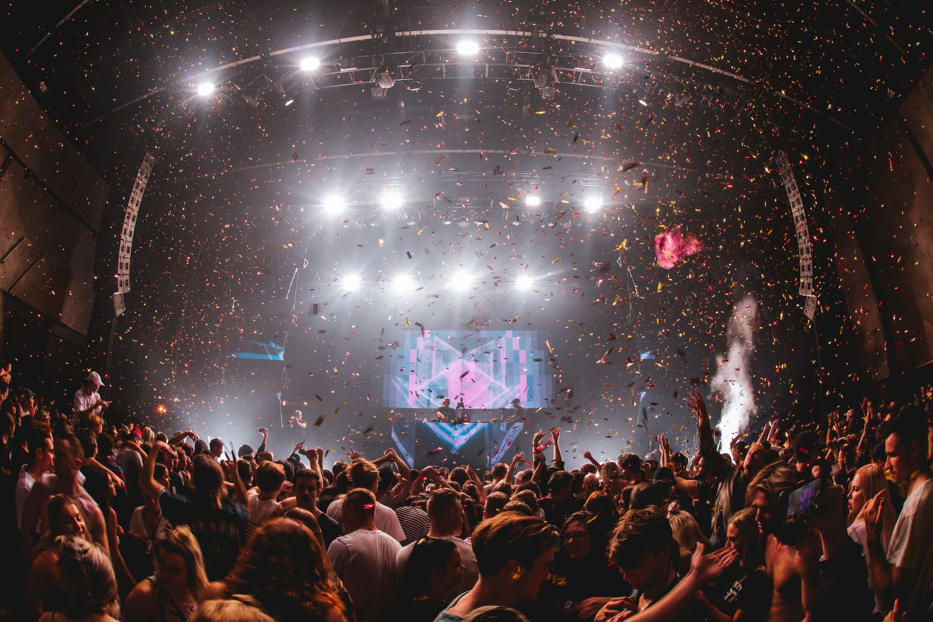 A crowd of people dancing under floating confetti in a concert hall.