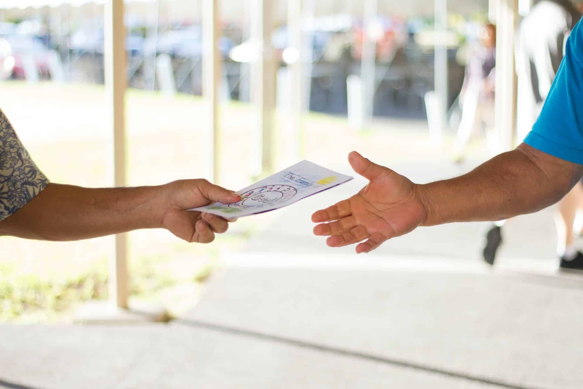 A person in a print short-sleeved shirt handing a flyer to a person in a blue short-sleeved shirt