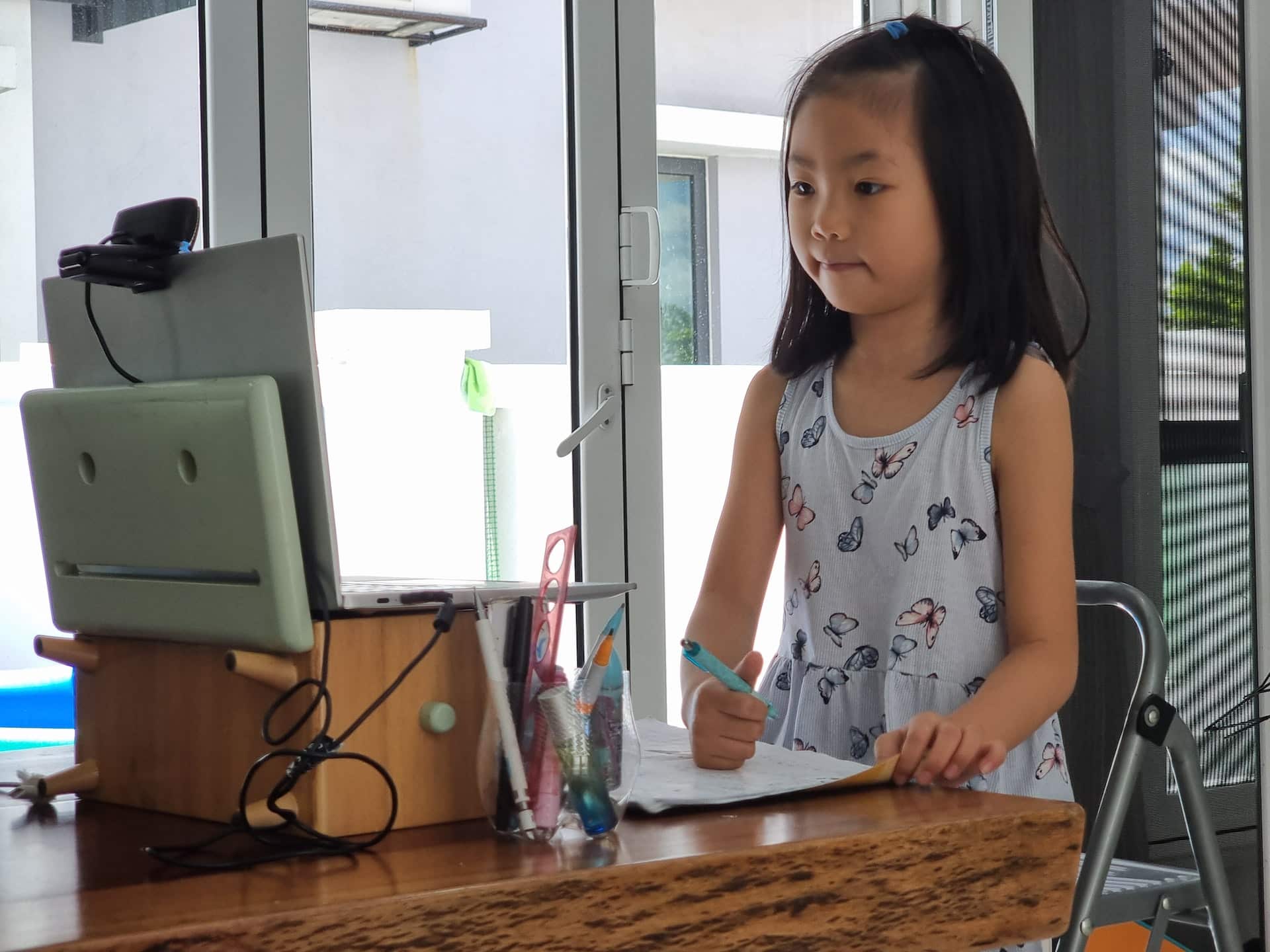 A young student standing in front of an open laptop with a pencil in hand
