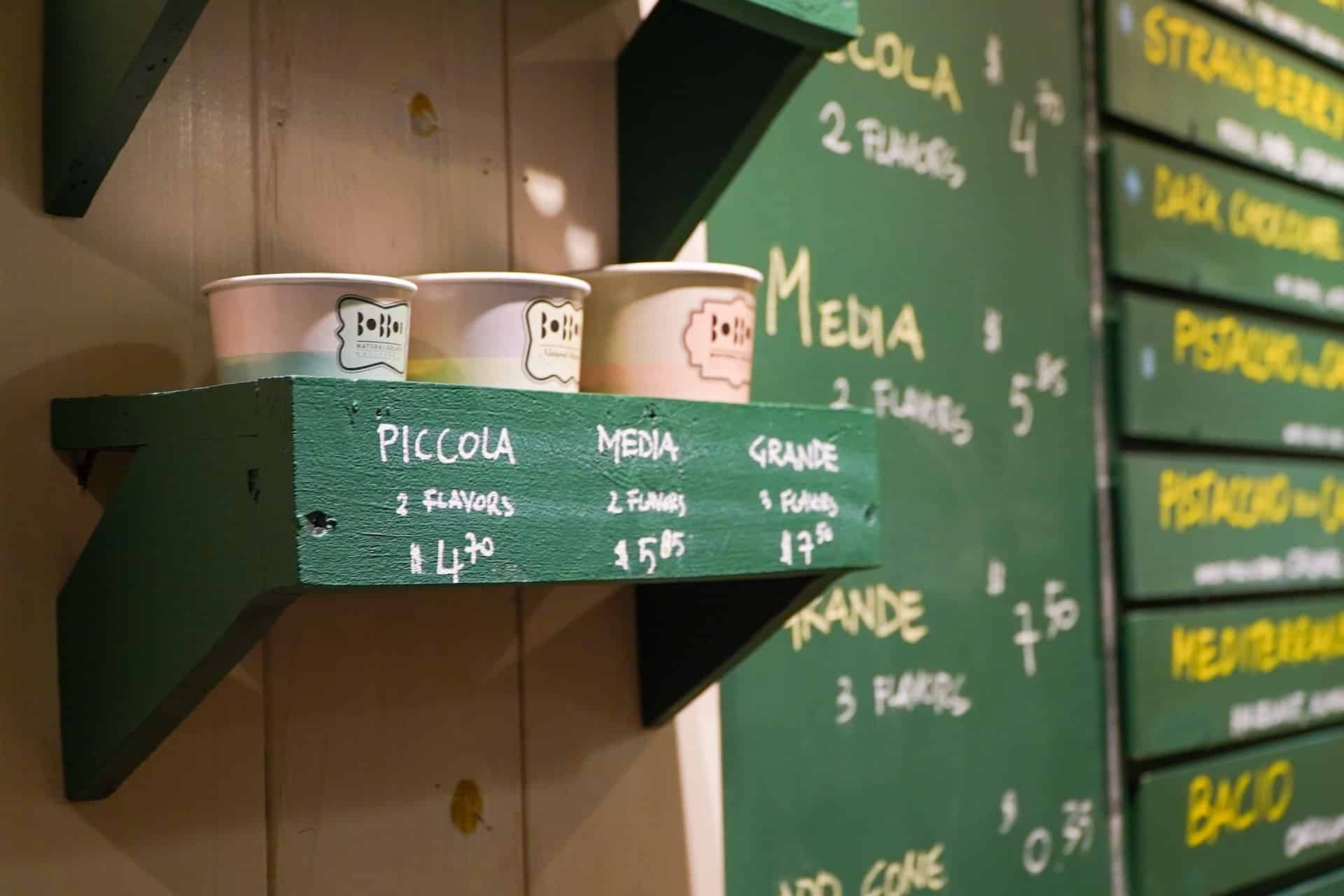 Three cups of progressively bigger sizes mounted on a green cupholder with a green menu board behind them.