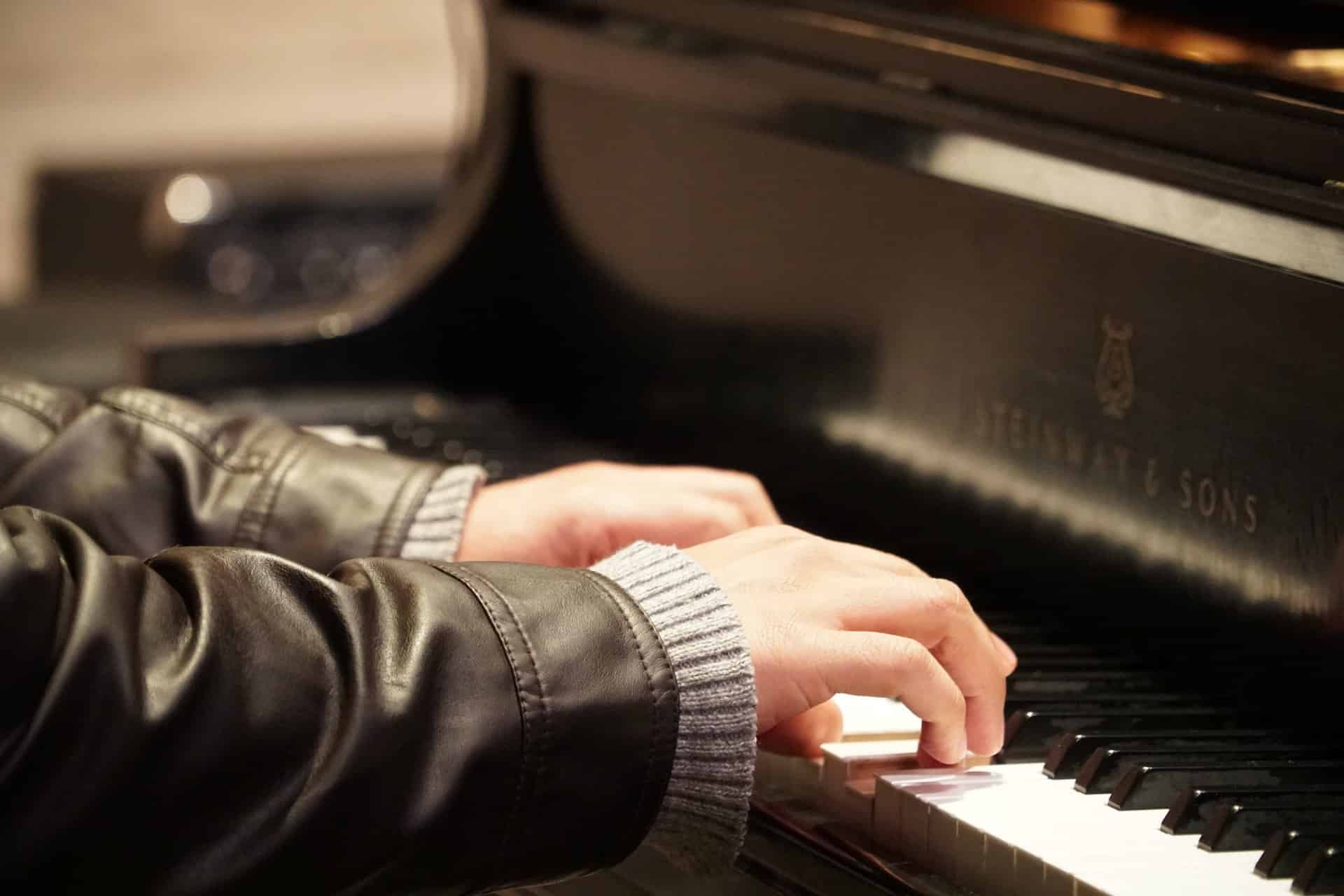 A person wearing a brown leather jacket over a knit sweater with their fingers on piano keys