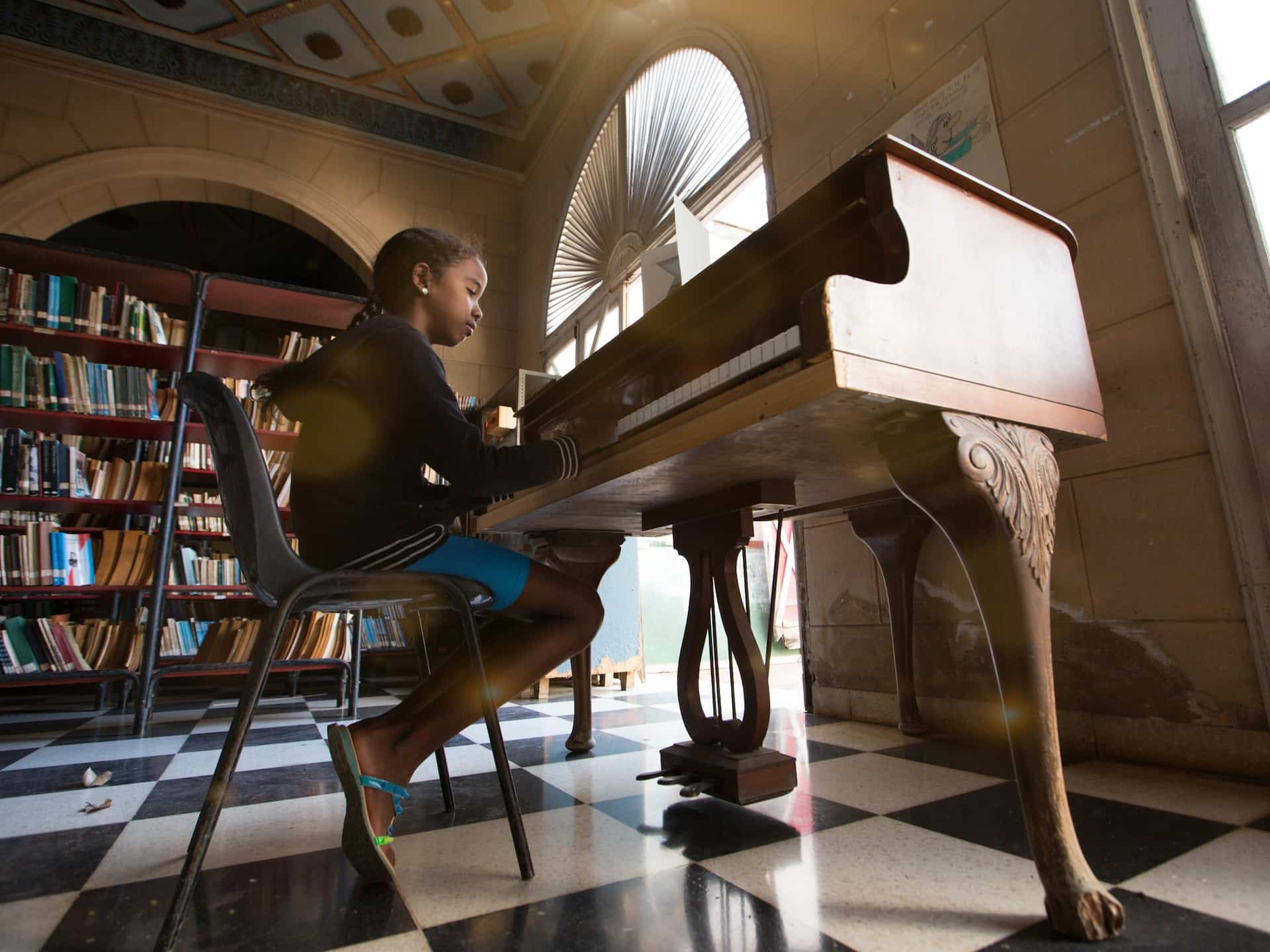 A young girl in a black hoodies sitting at a piano in a brightly lit room