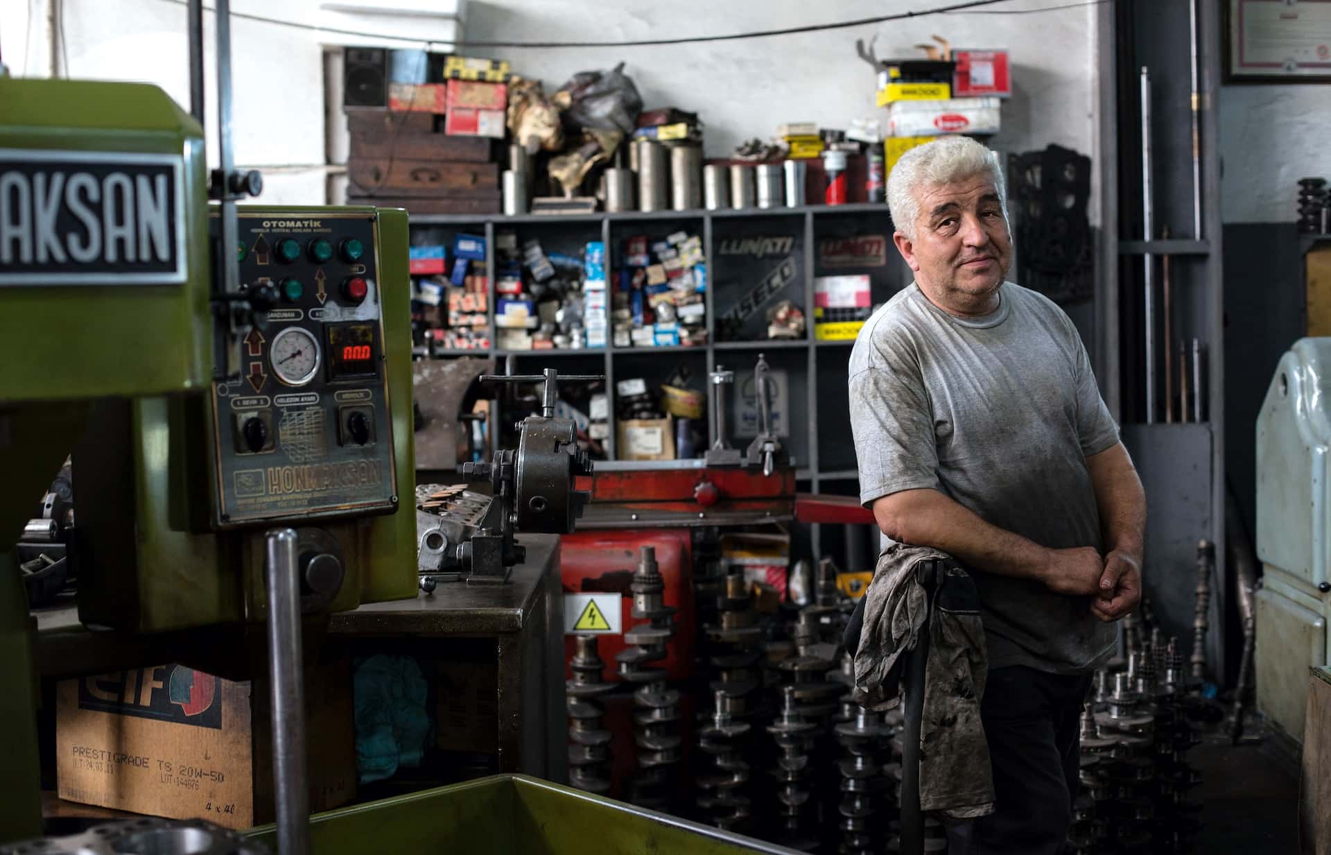 A man in a grey tee-shirt in a mechanics shop with a hydraulic press in the foreground