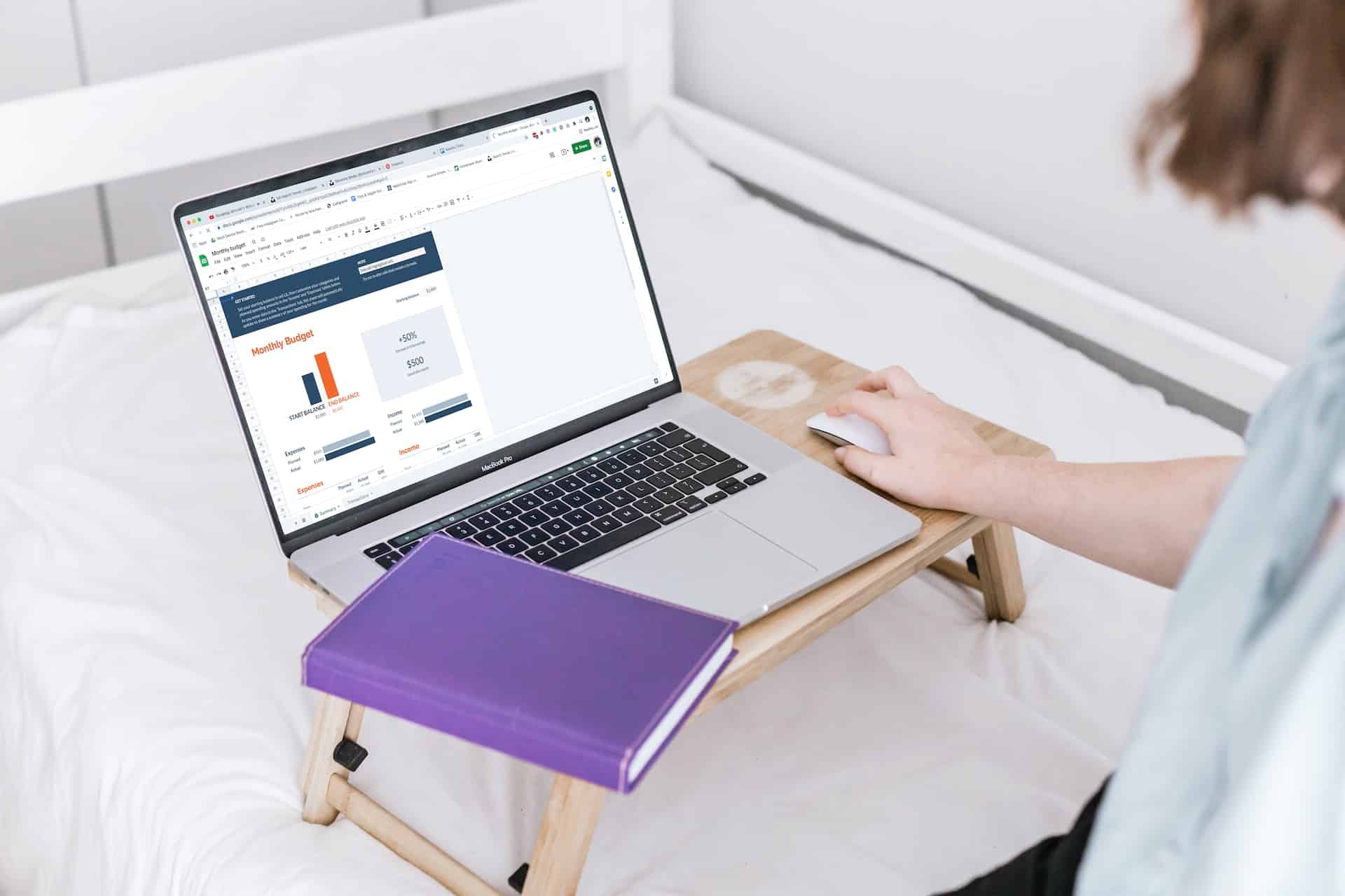 A person in a light blue shirt looks at an open laptop displaying a budget bar graph