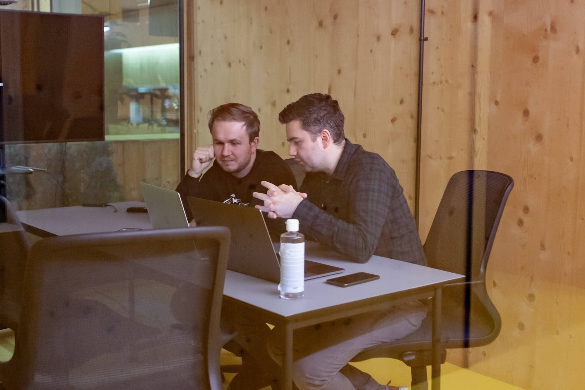 Two young men sitting behind a window at a desk in a wood-panelled room.