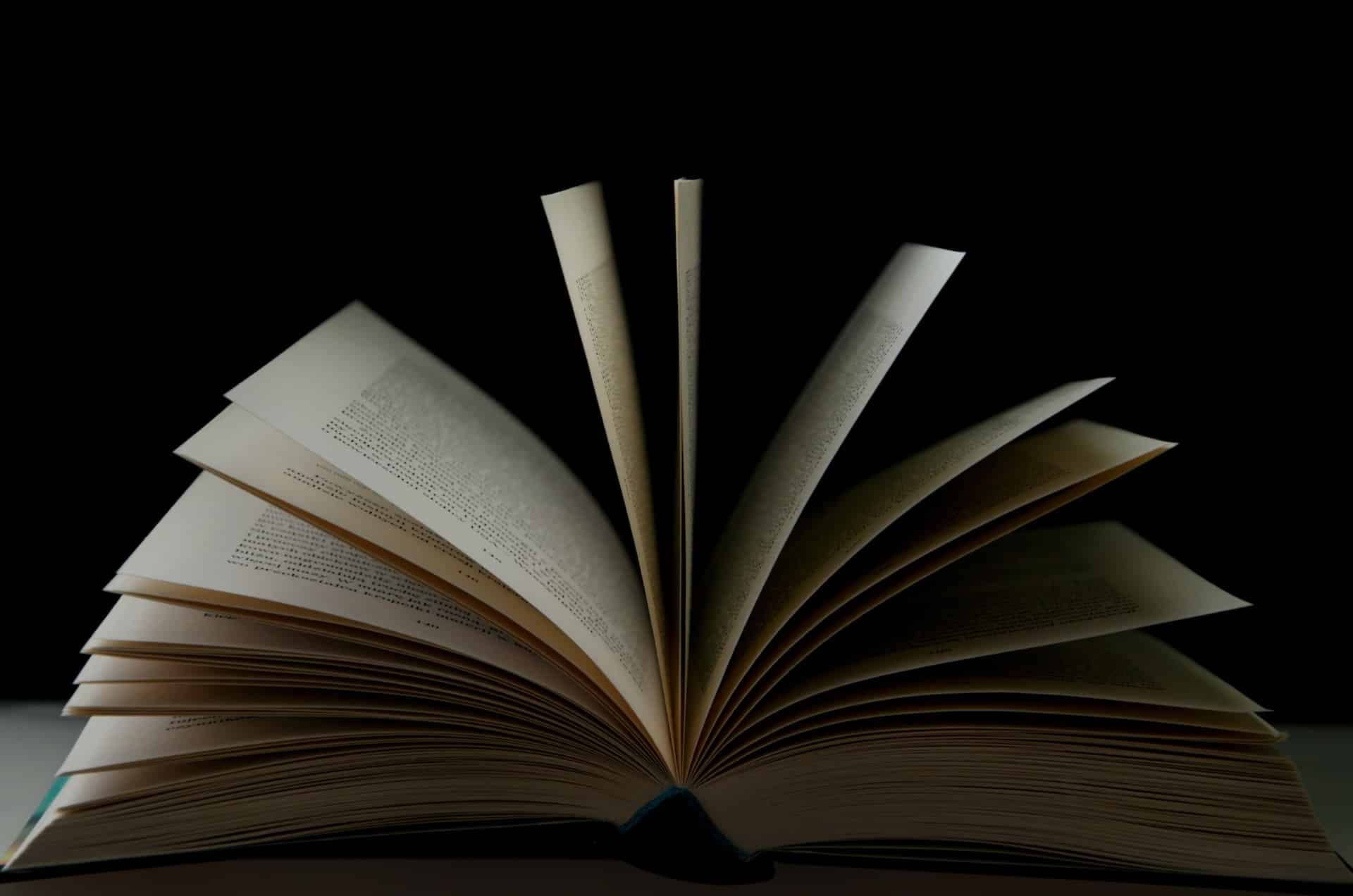 An open book with its pages fanned out in a half-circle against a dark background