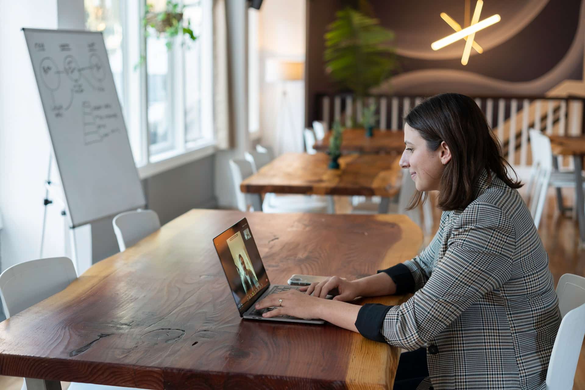 A woman in a grey cardigan videochats with a student while sitting at a long, wooden table.
