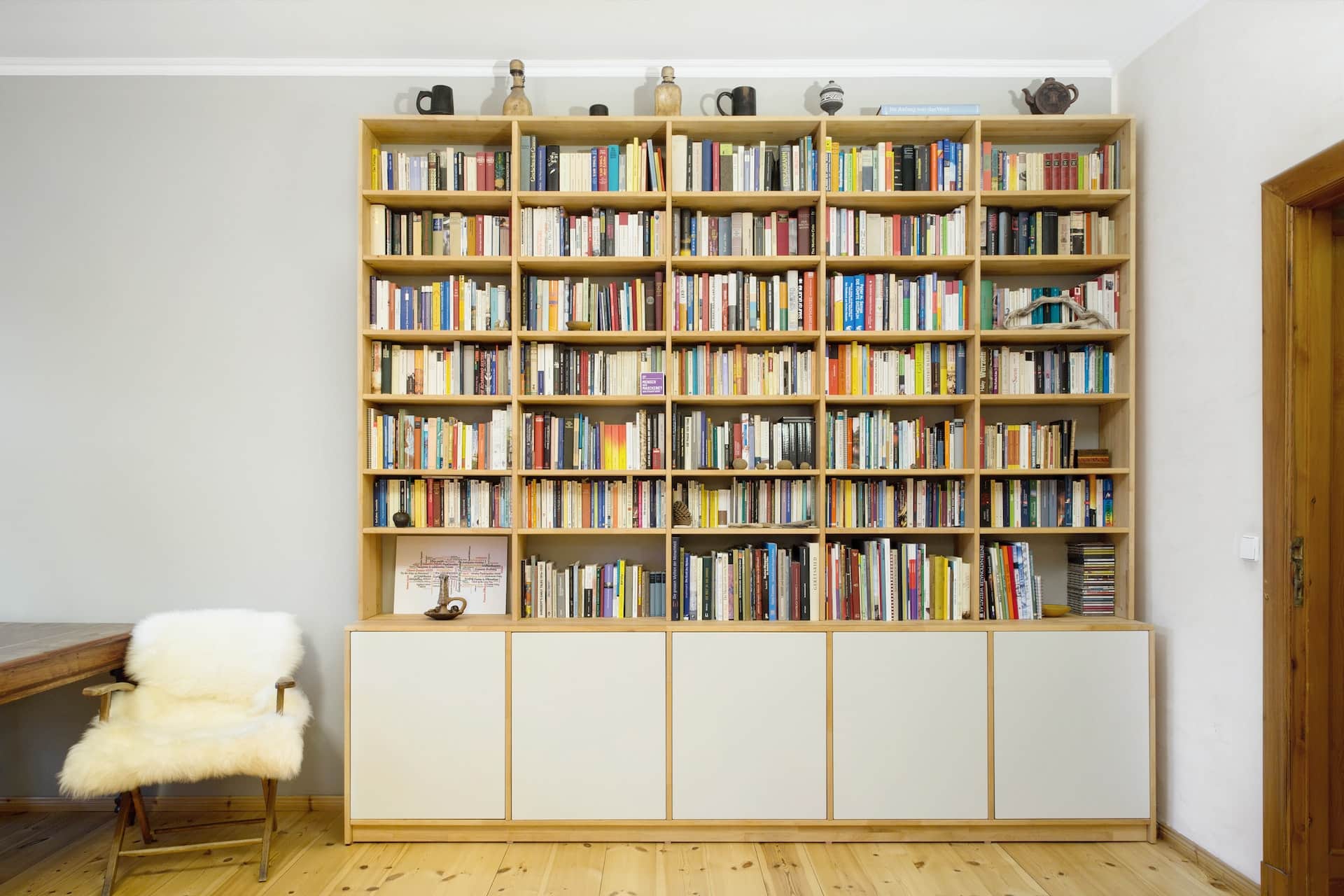 A fully laden bookshelf positioned against a white wall in a brightly-lit room.