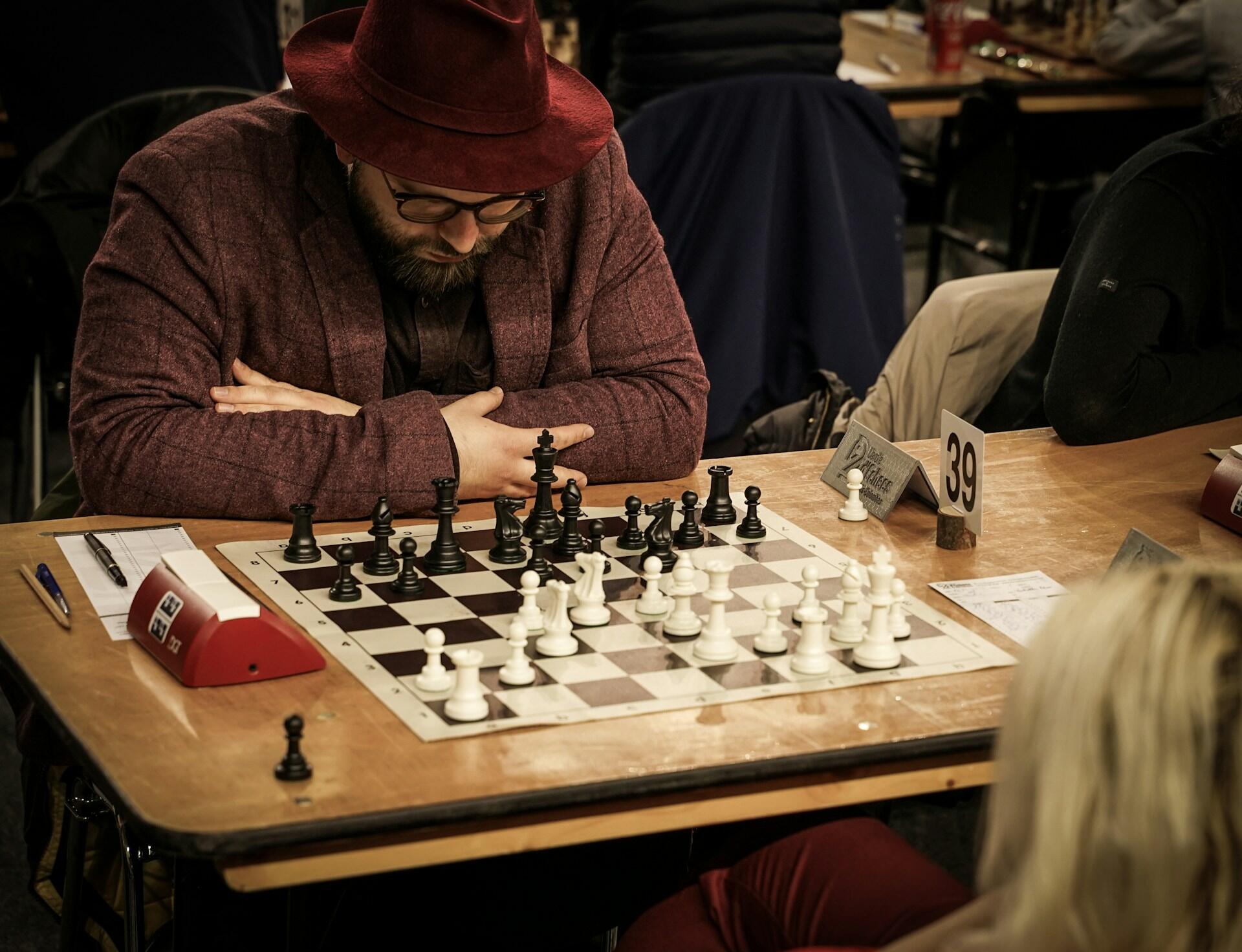 A person wearing a red hat contemplates a chess board.