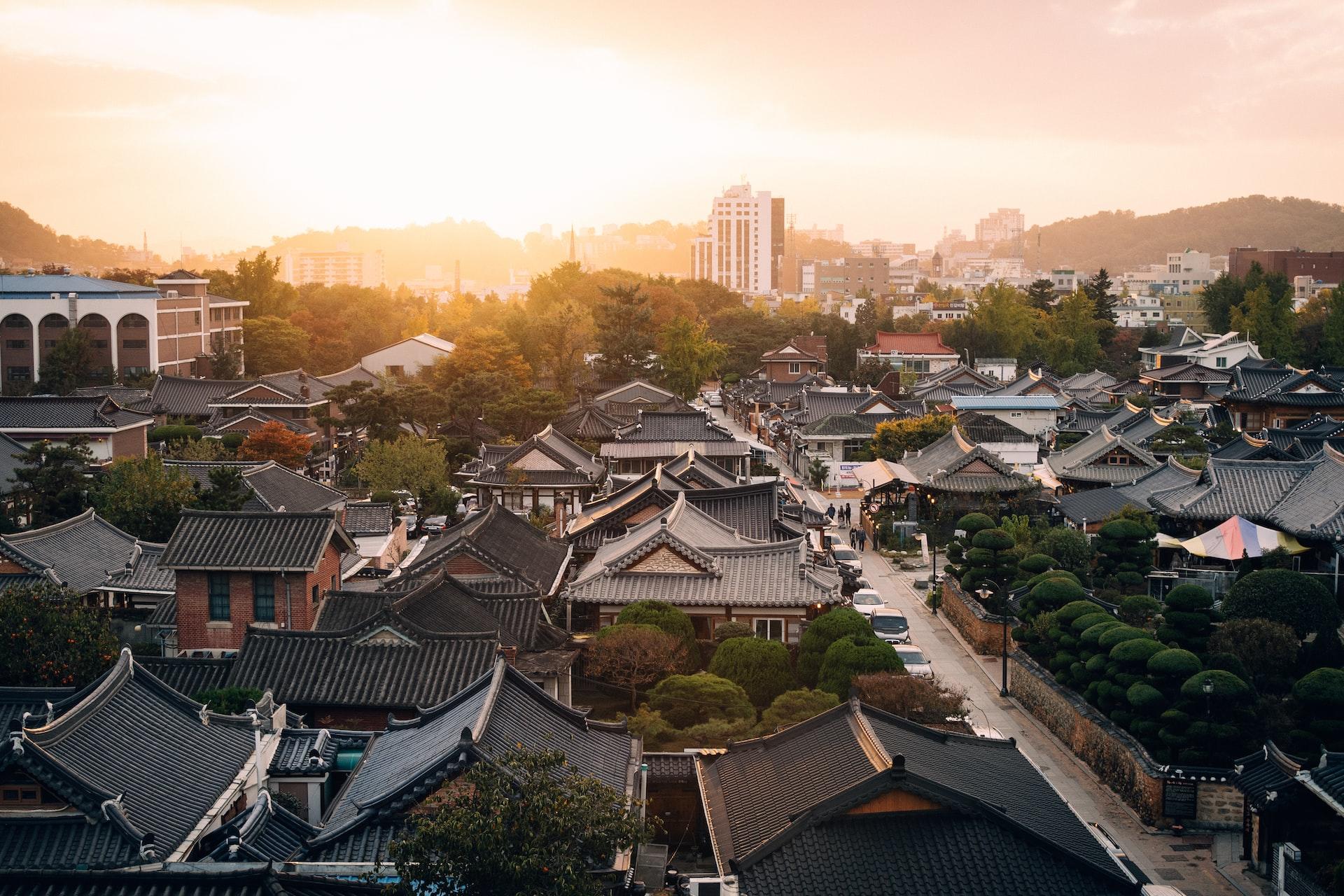 Sunrise in South Korea over a neighbourhood of traditional architecture, low-rise houses with a modern tall building in the background
