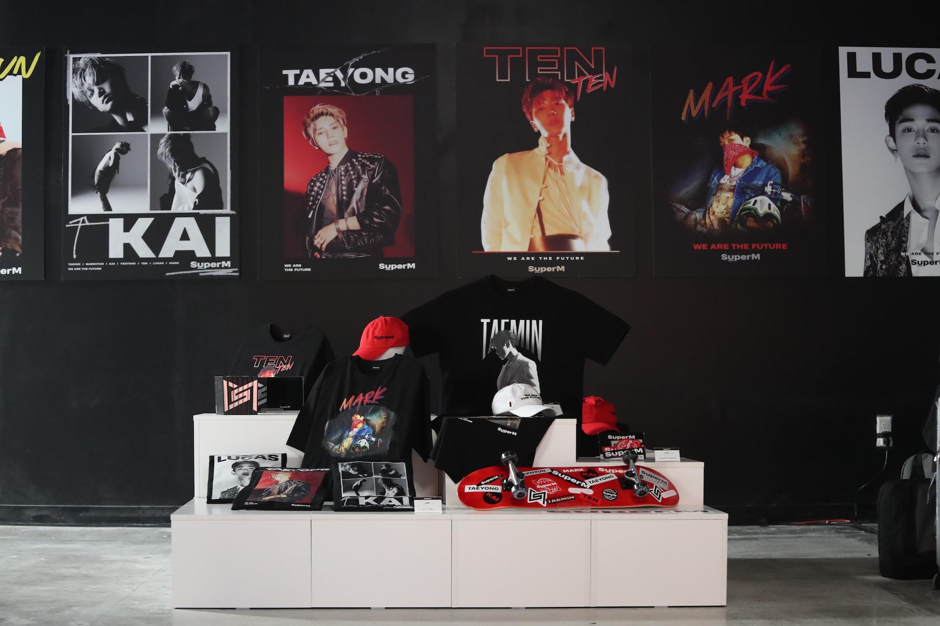 A merch display on a white platform in front of several K-pop idol posters.