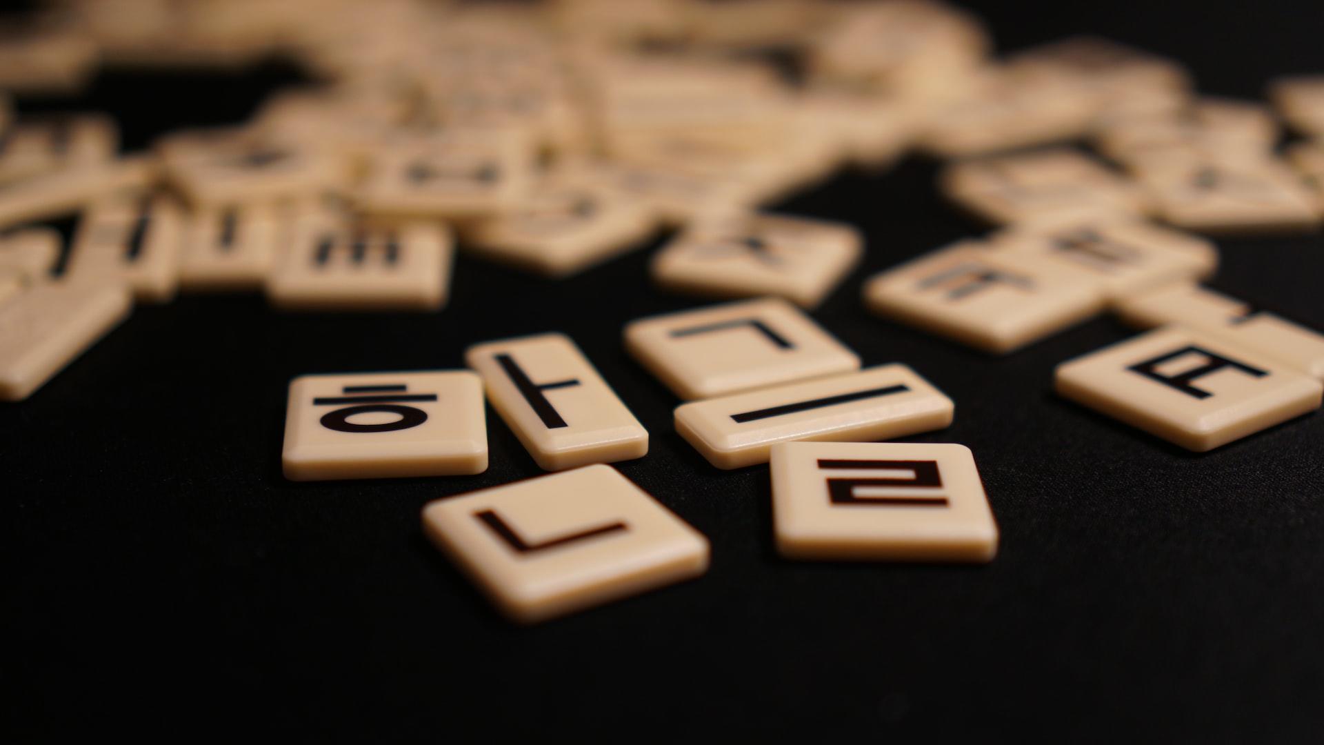 A group of blond wood Korean letter tiles printed in black ink scattered on a black surface.