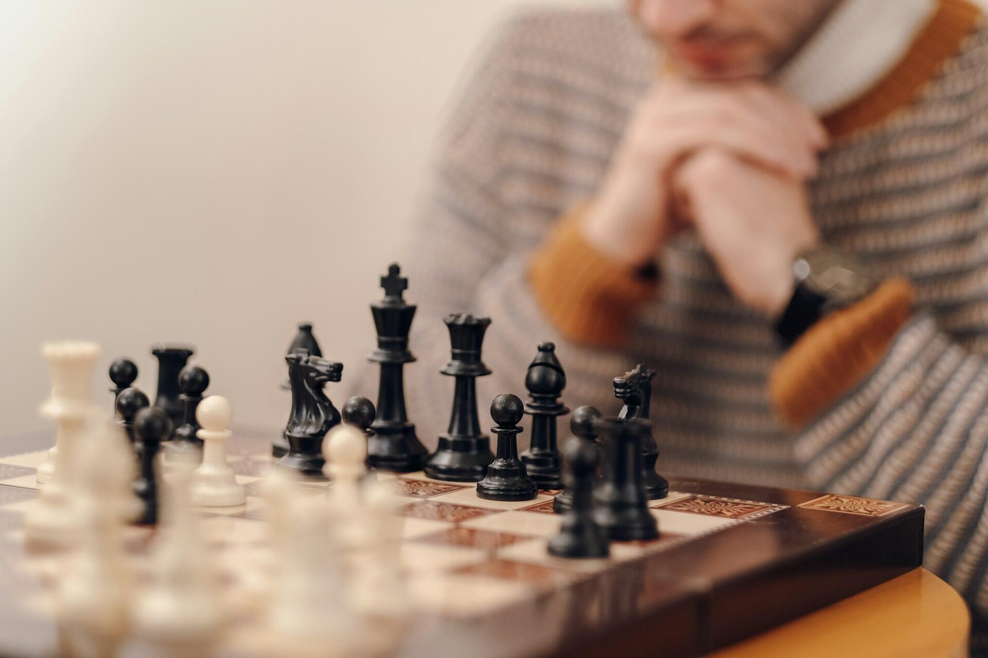 A person in a striped jumper contemplates a chess game in progress.
