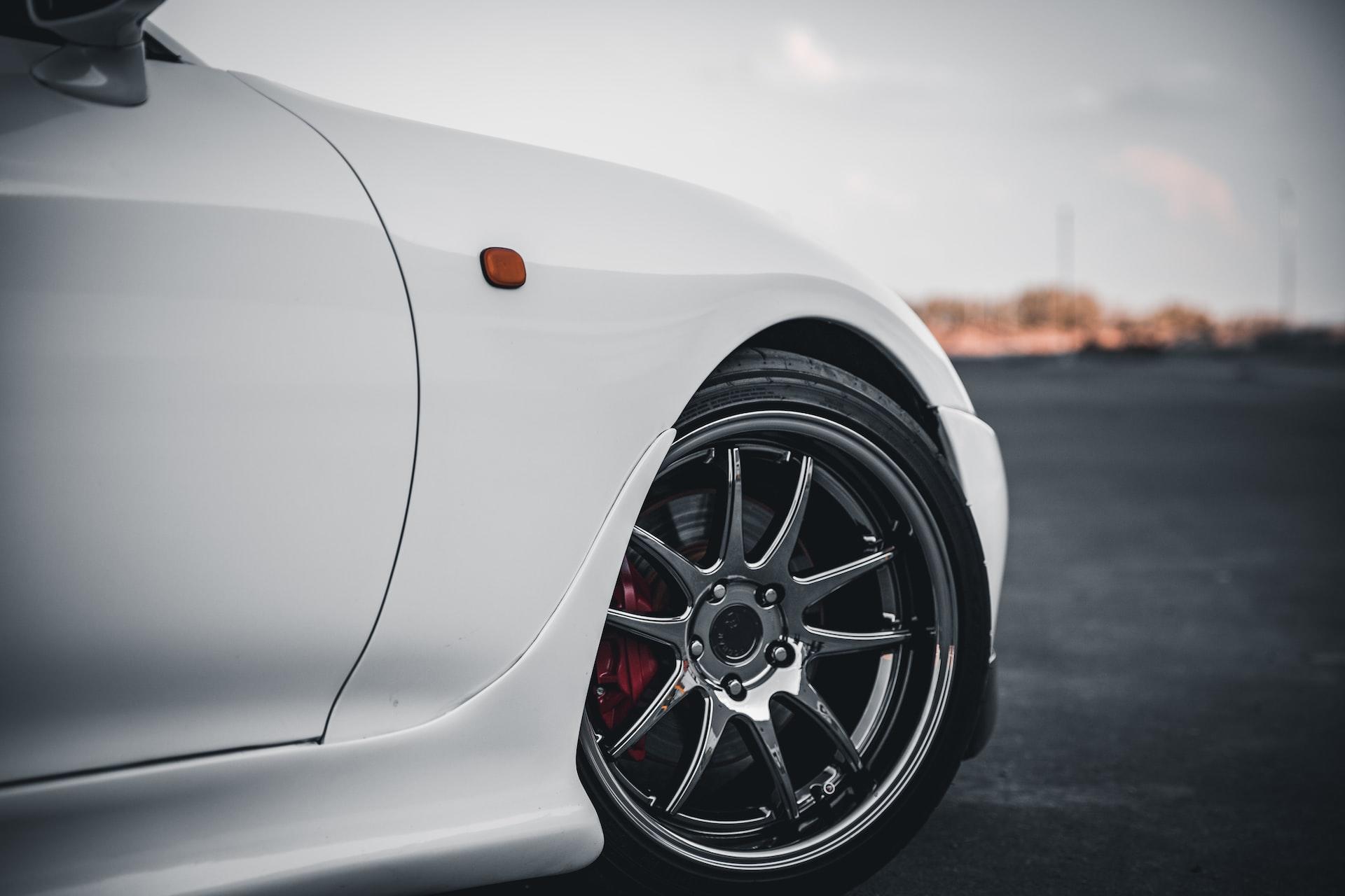 A close-up of a white car's right front wheel showing the red brake caliper through the spokes of its rims.