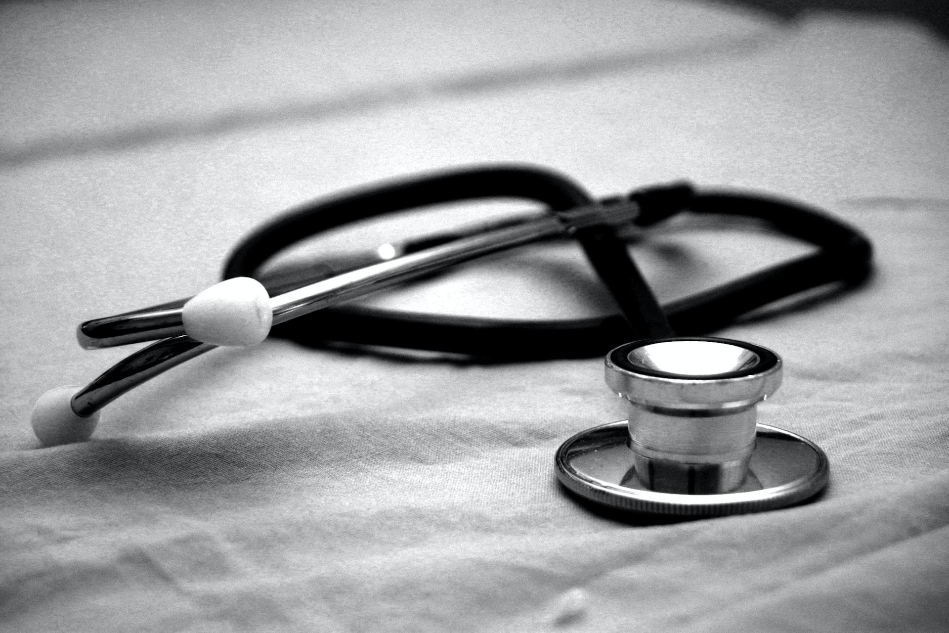 A black and white snapshot of a coiled-up stethoscope resting on a light-coloured surface.