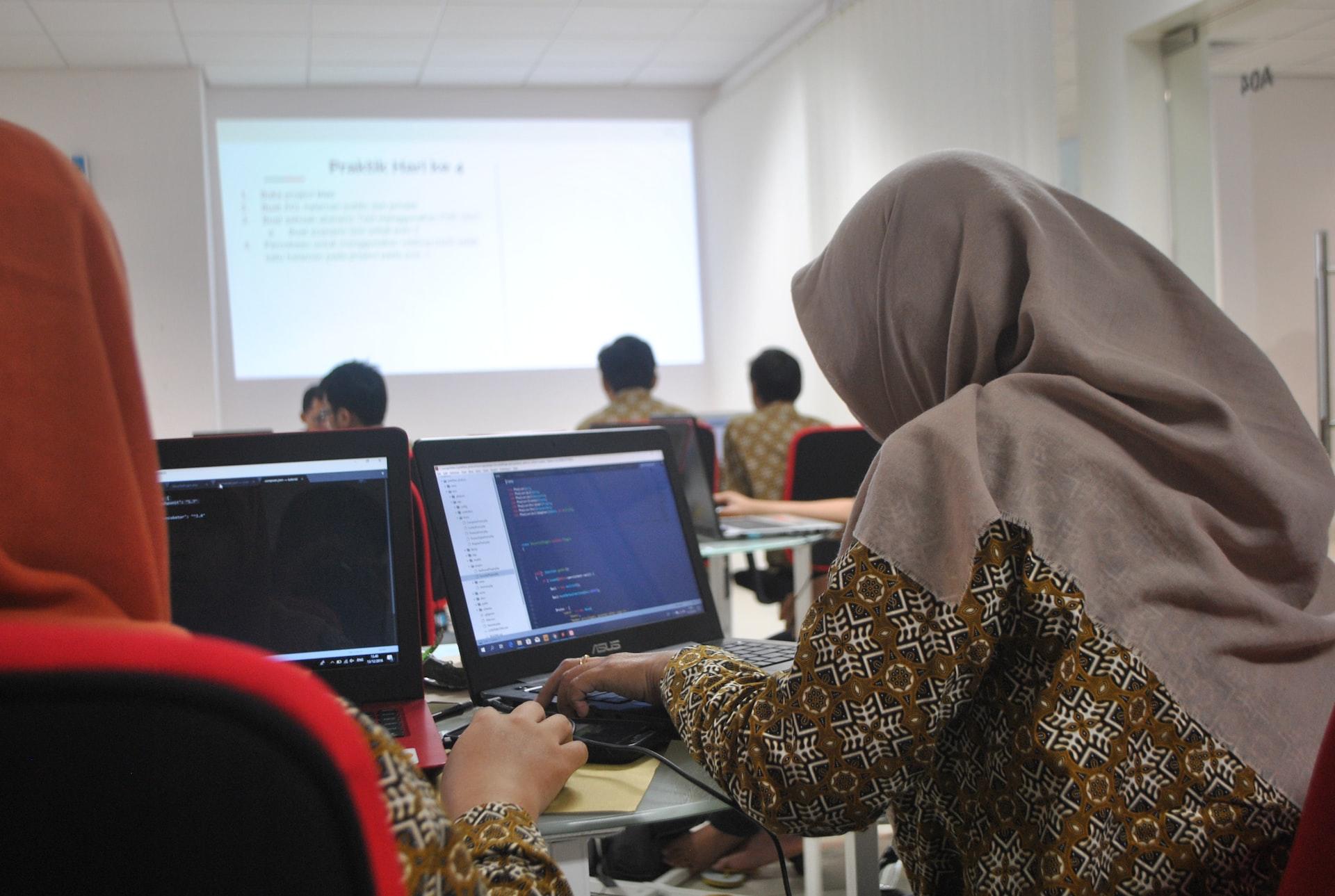 A woman in a grey hijab learns how to code in a coding class