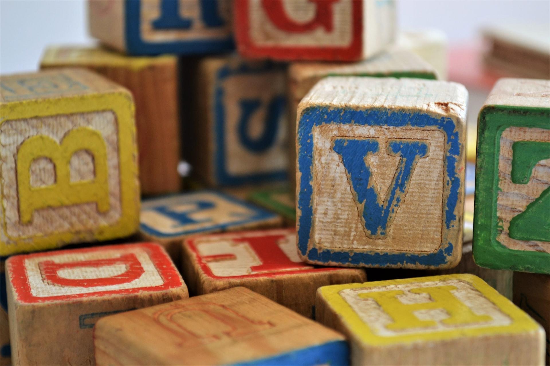 A collection of wooden children's play blocks displaying various letters in various colours, with V and B most prominently displayed. 