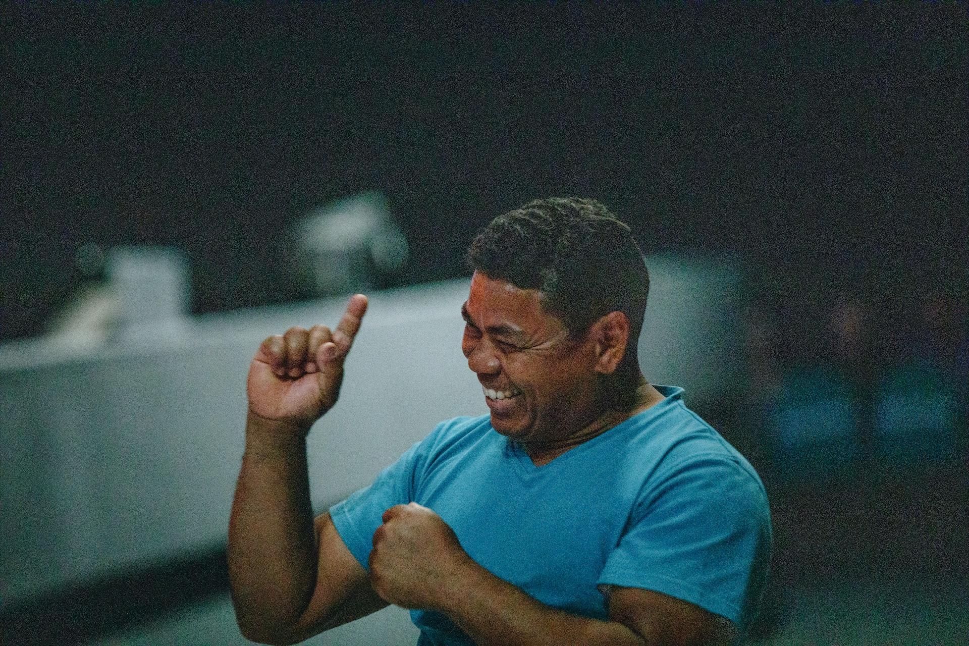 A man in a blue t-shirt smiles as he communicates in sign language.