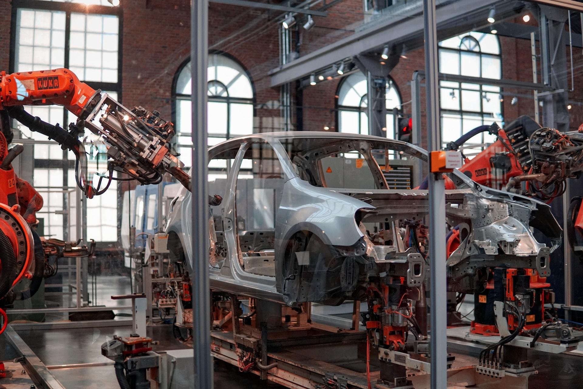 An automobile production line featuring a half-built car with an orange robotic arm poised to work on it.