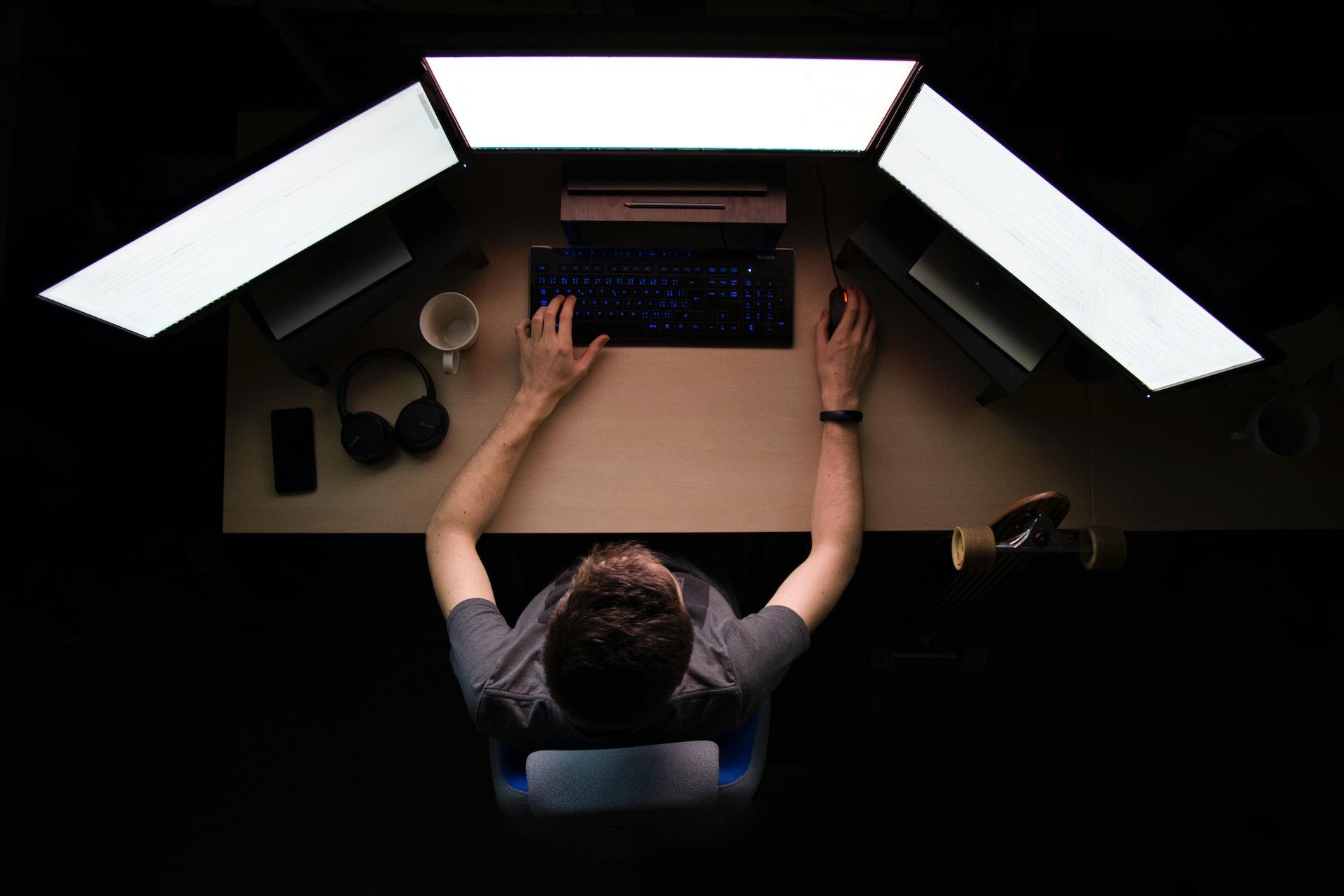 An overhead view of a person sitting in front of a three-monitor setup, typing on a keyboard. 