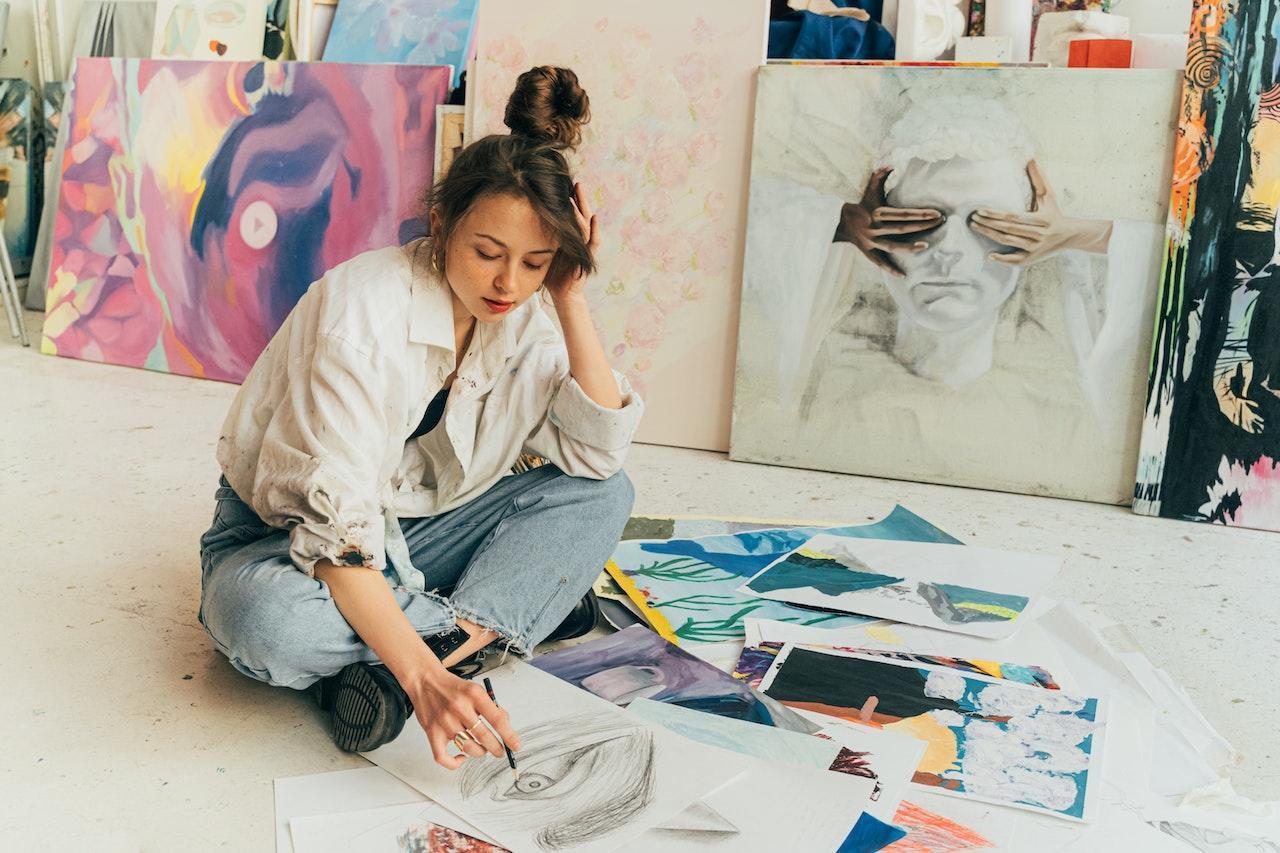 A student artist sketches a portrait while surrounded by other examples of her work.