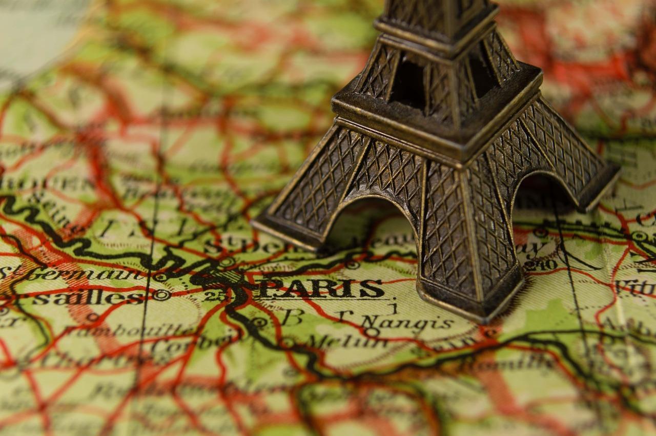 A mini Eiffel Tower souvenir sits on top of Paris marked on a map.