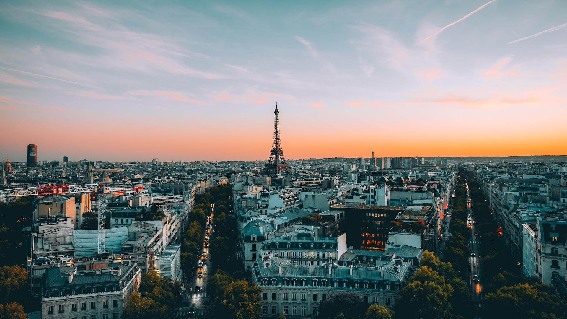 Aerial view of Paris at sunrise showing the Eiffel tower and the city against a blue and orange sky.