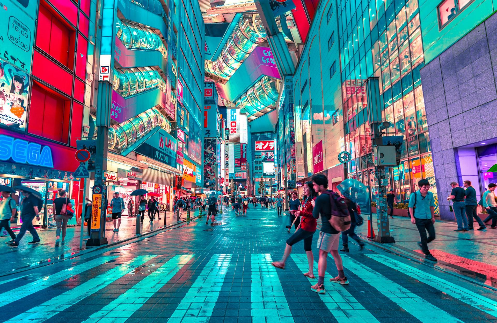 Vibrant city street with pedestrians, neon signs, and colorful reflections on wet pavement.