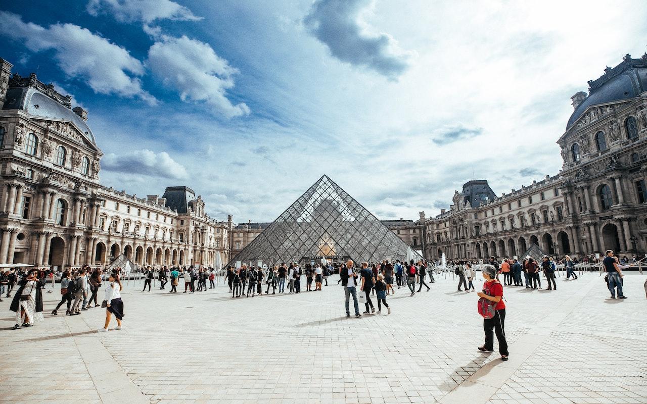 The pyramid of the Louvre on a sunny day with people walking around outside in the courtyard.