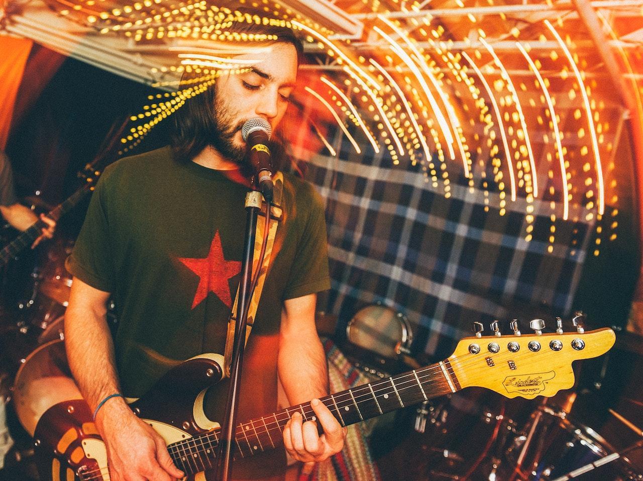 A man plays the guitar and sings into a microphone. A photo effect is at the top half of the photo, which is a long exposure of lights creating a blurred-light effect.