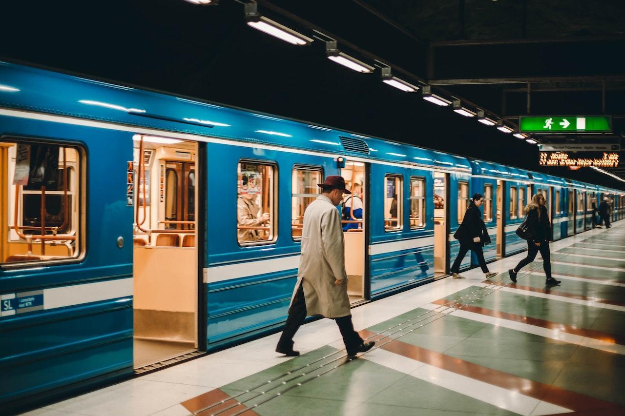 A metro train is stopped at an underground station while people get on and off through the open doors.