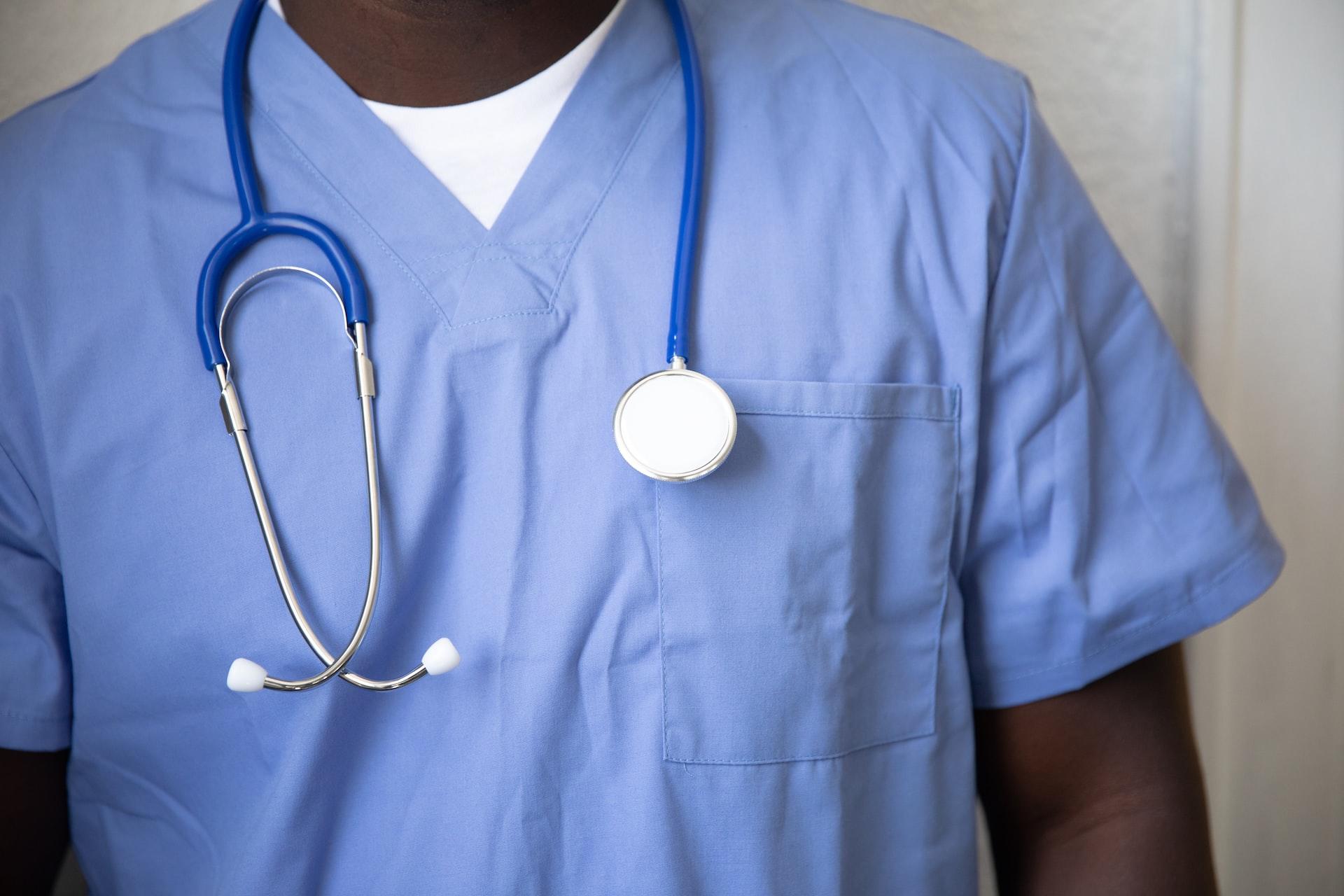 A nurse wearing blue scrubs with a stethoscope around his neck