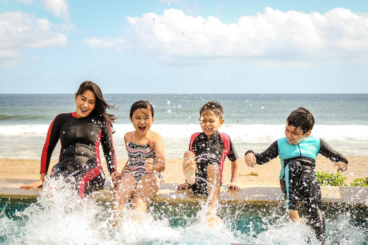 A swim instructor splashes the water with young students by kicking in the pool.