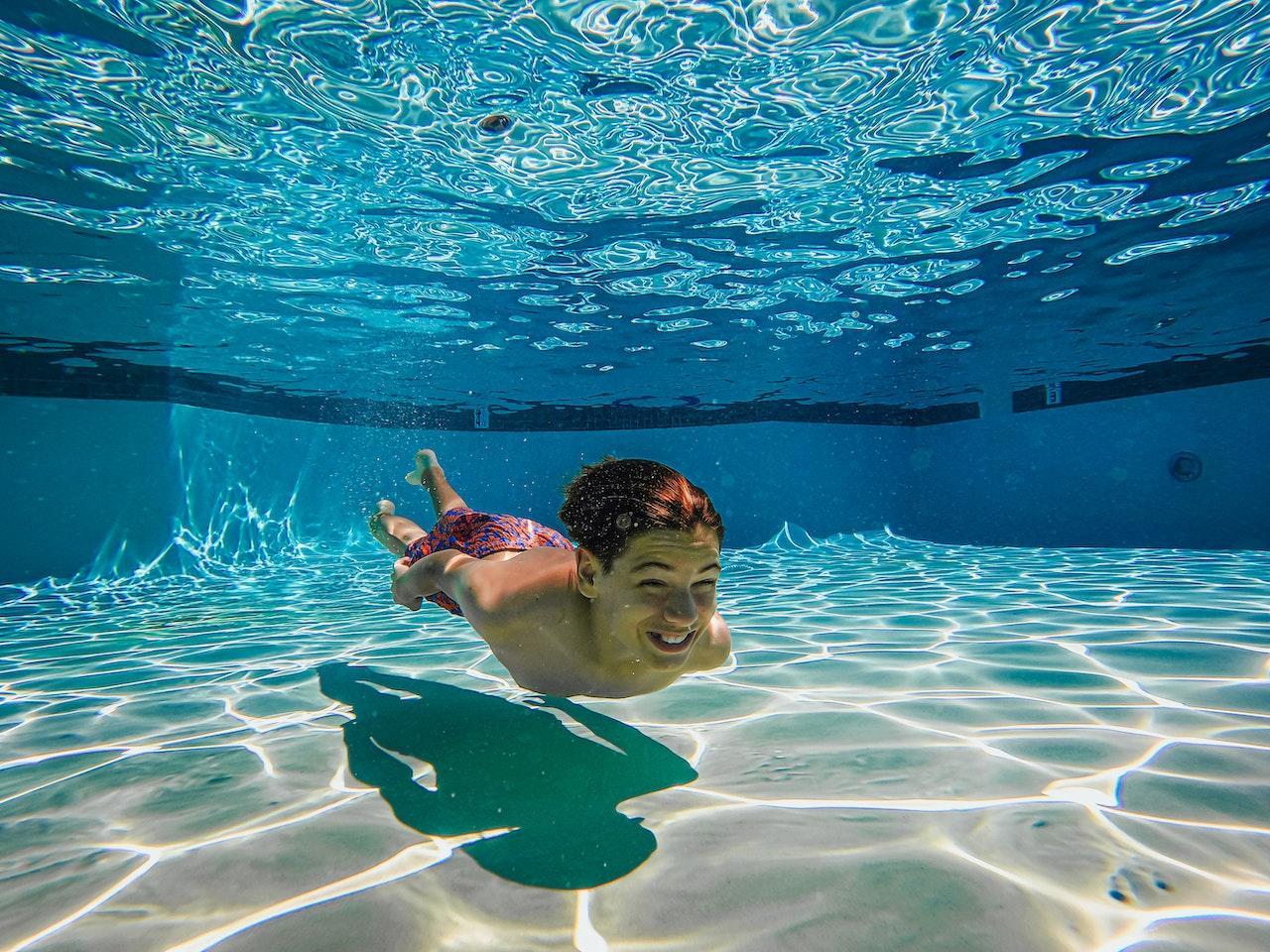 A young adult swims underwater in a pool with their eyes open.
