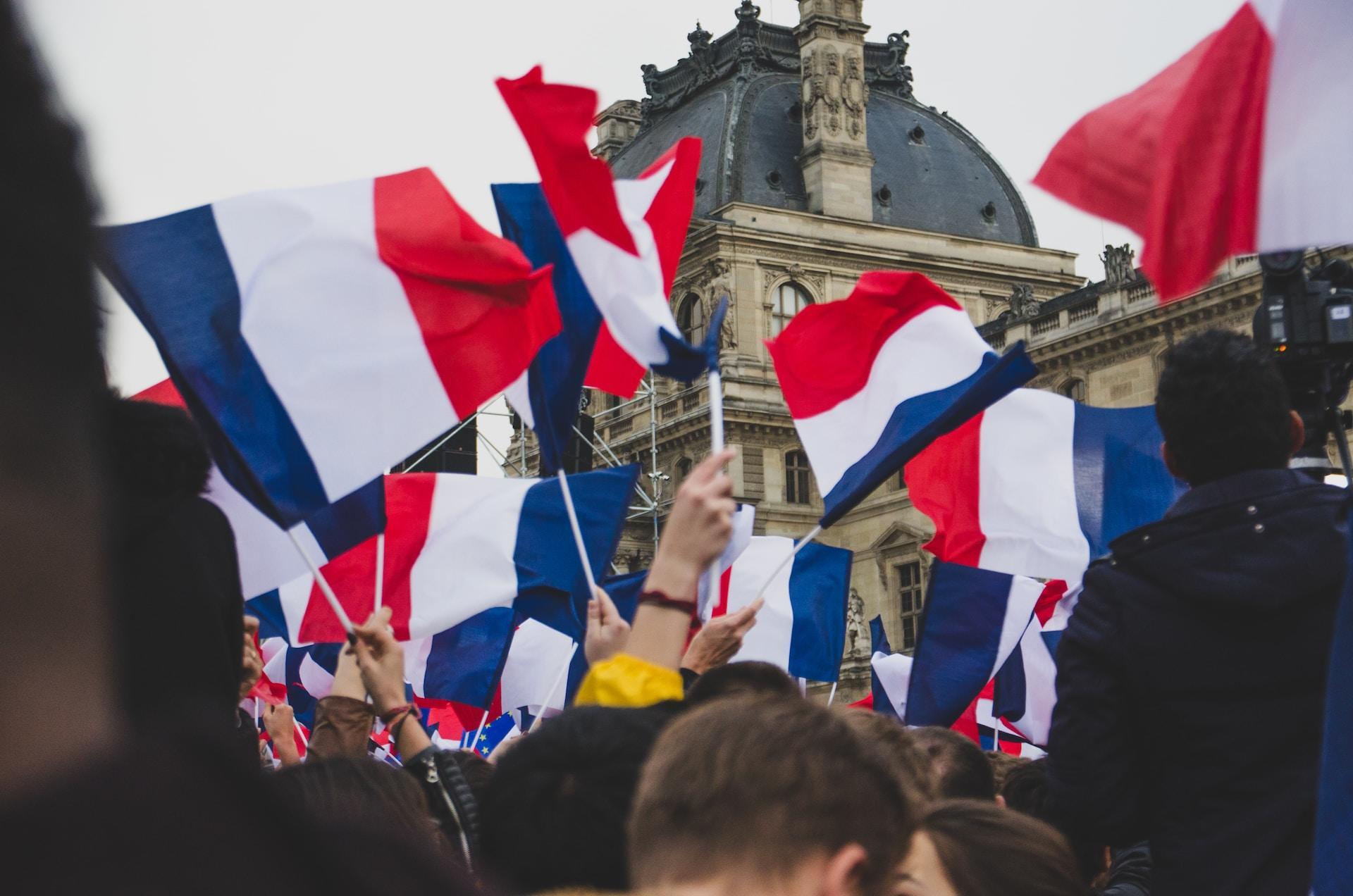 A crowd holds up many French flags on sticks.