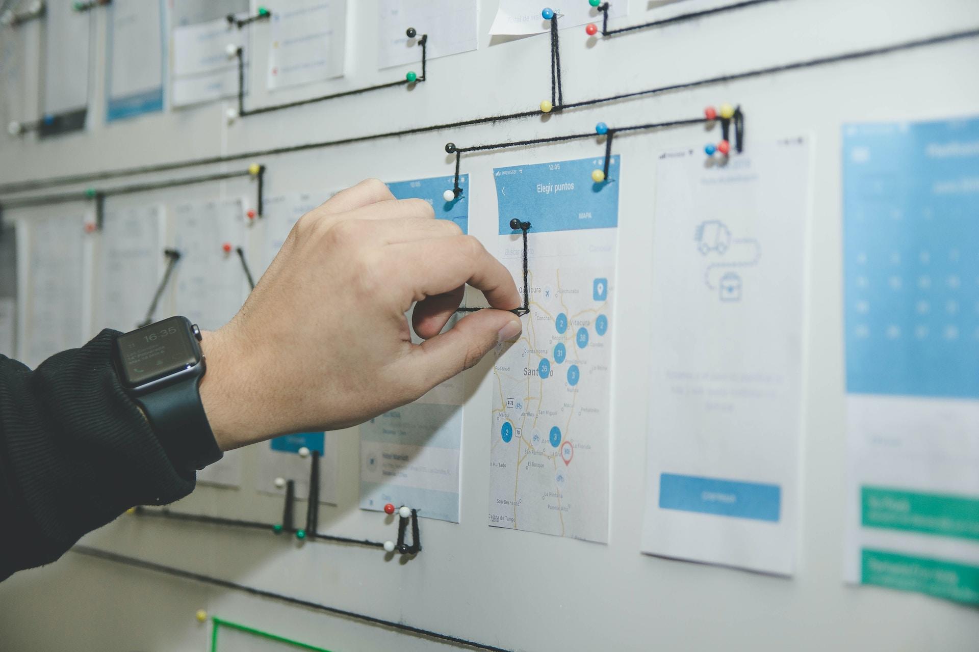 A person wearing a dark, long-sleeved top pushes a pin into a wall of mapped information.
