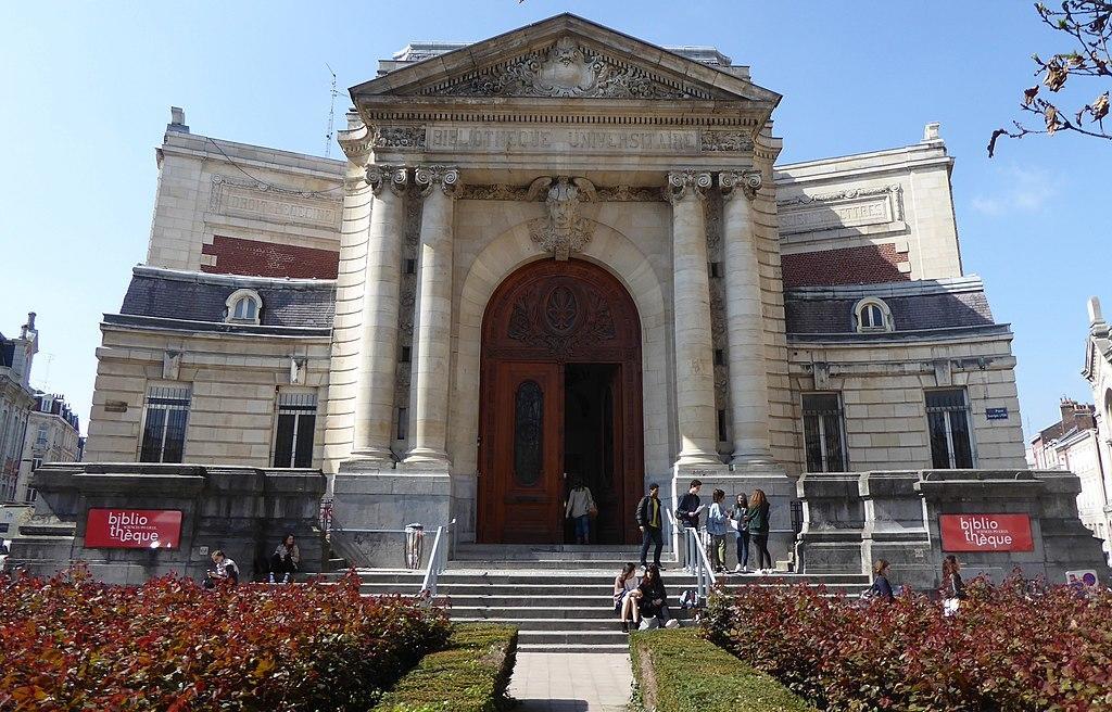 The Sciences Po library building which has an enormous archway with columns and some students sit on the stairs in front.