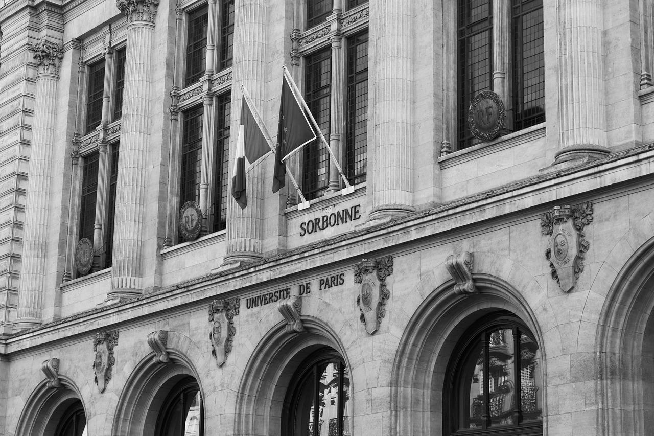 The front facade of Sorbonne University showing historic brickwork and flags hanging above the archways.