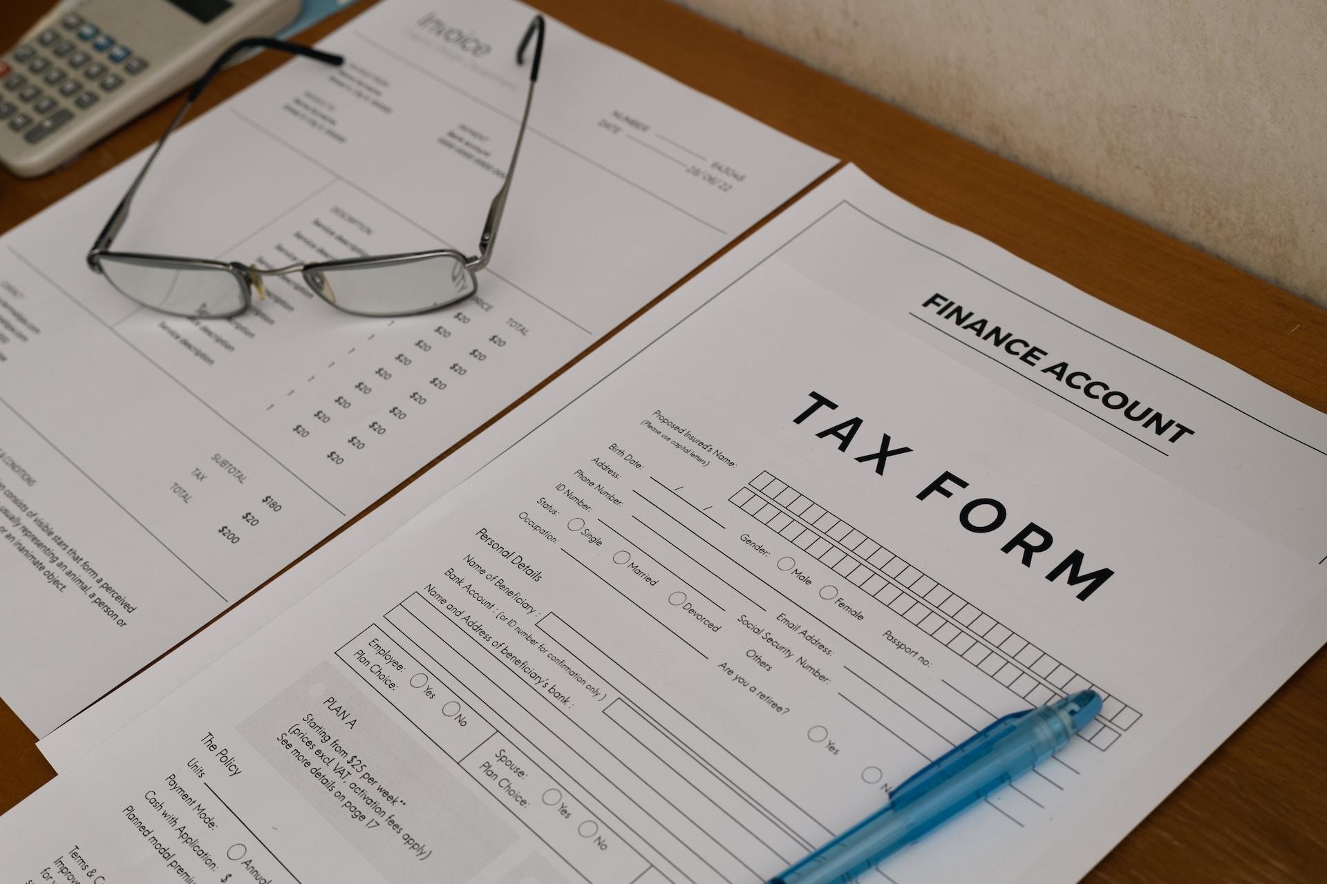 A dark brown file folder open to reveal a tax form with no data filled inn and an accounting document, upon which rests a pair of eyeglasses.