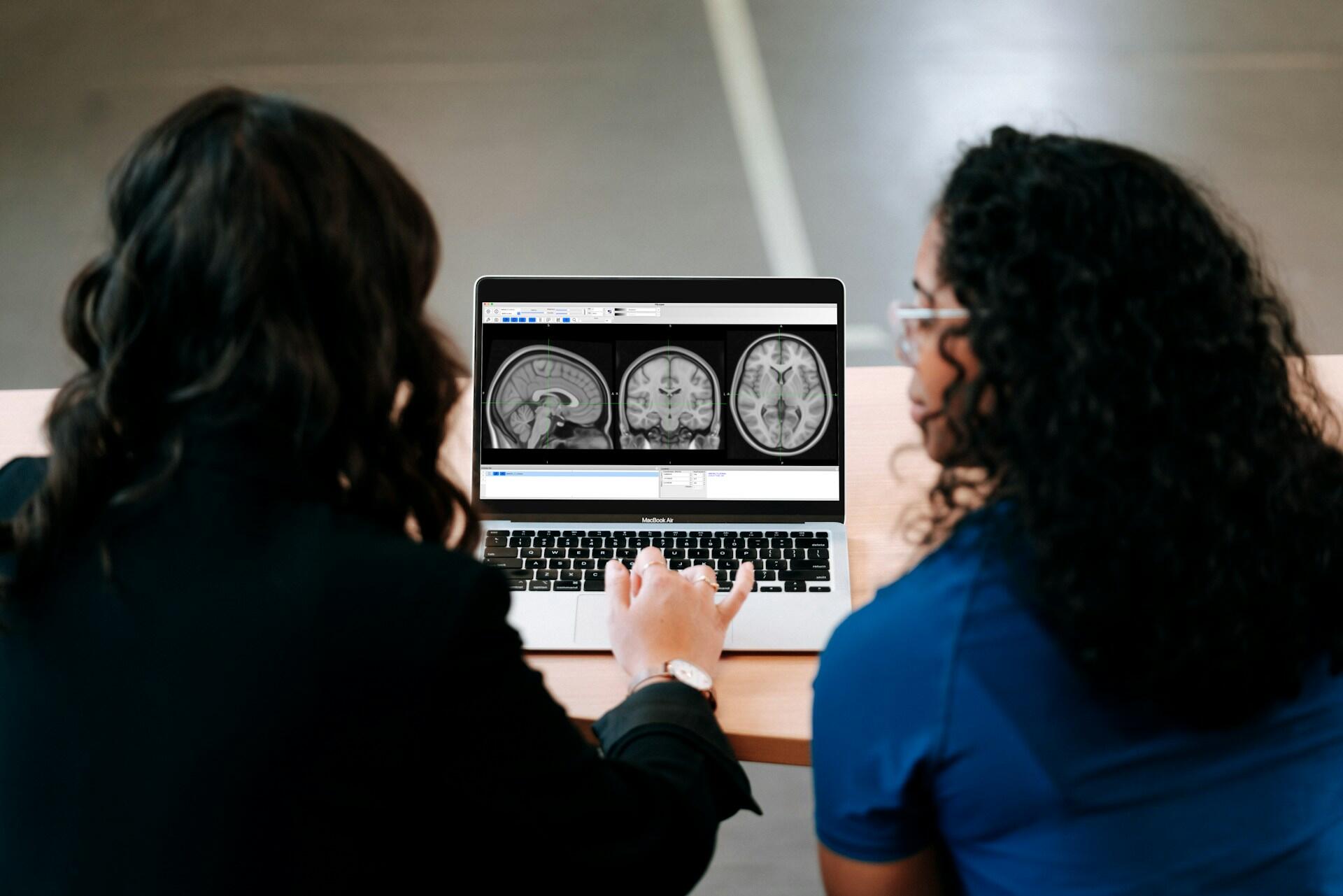 two scientists looking at images of a brain on a laptop