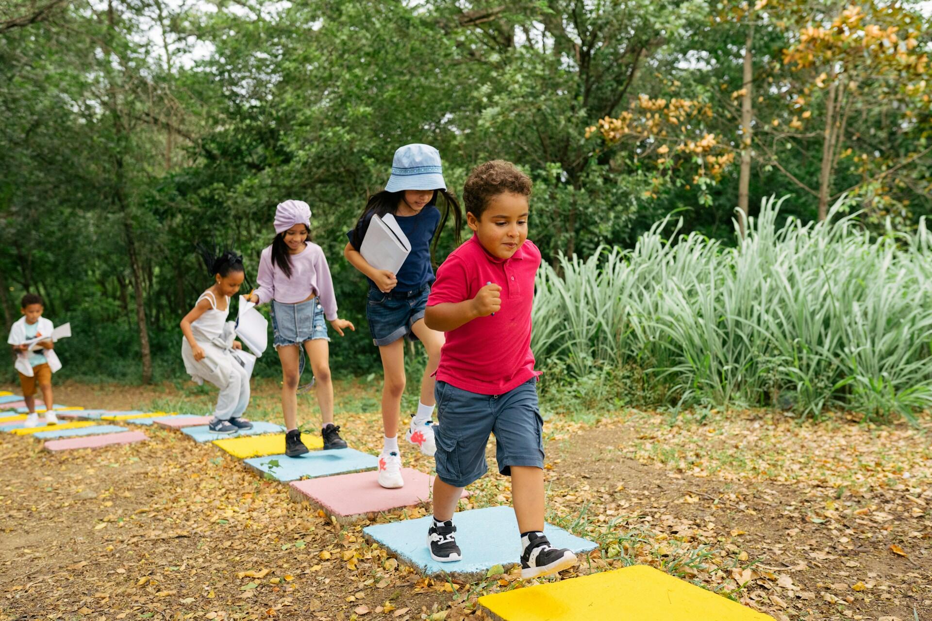 young children playing outside and jumping on colourful concrete squares on a forest path