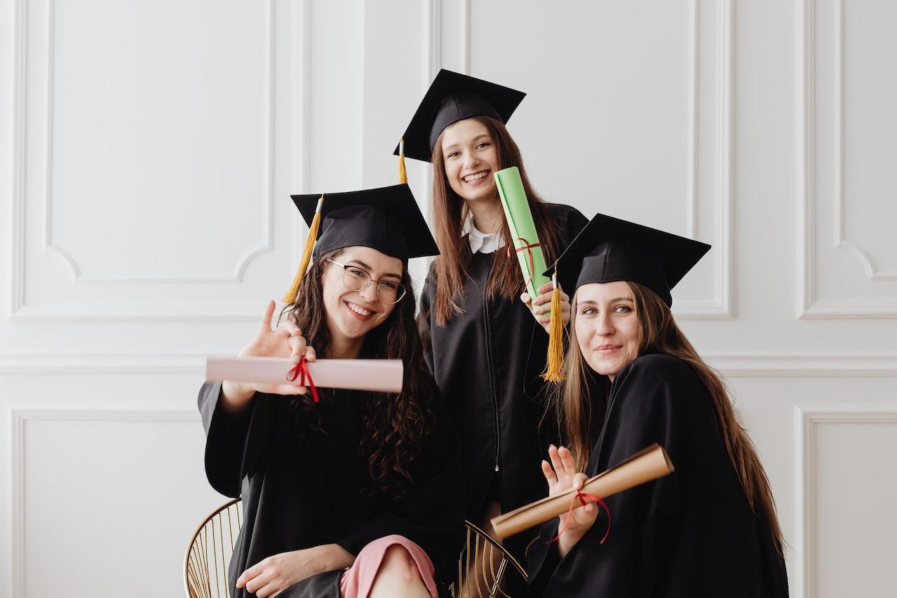 Three students posing in their caps and gowns holding prop diploma scrolls.