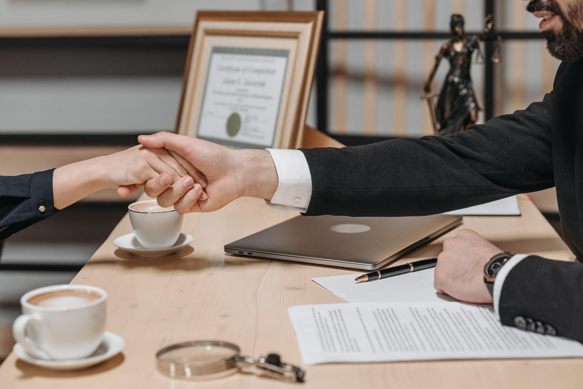 A client and her lawyer shake hands over a desk.