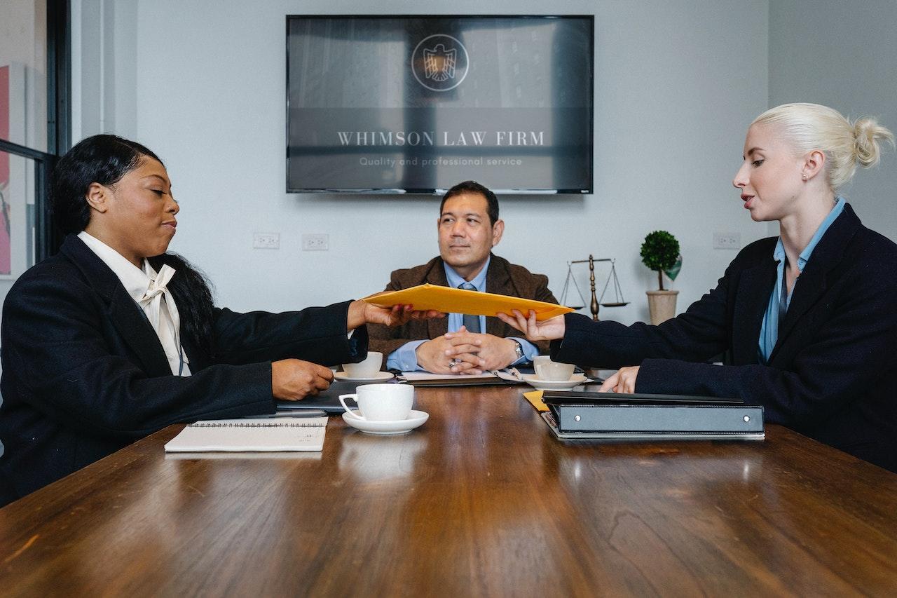 A yellow envelope of paperwork is passed from one person to another in a law conference room.